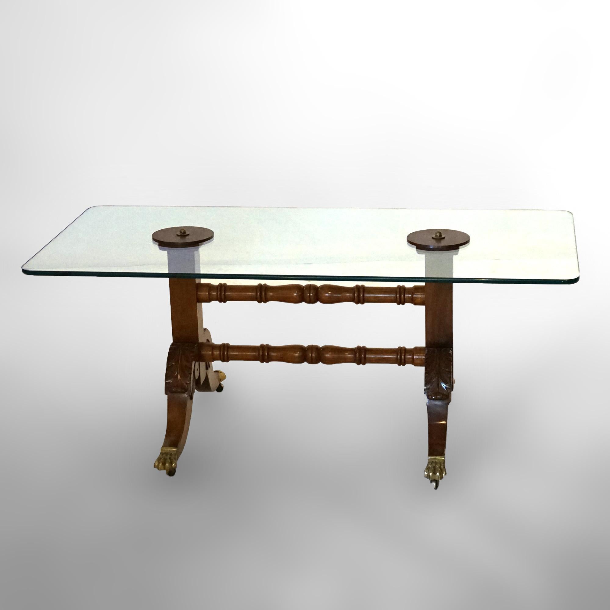 An antique low table in the manner of Duncan Phyfe offers glass top over trestle style base having foliate carved legs with turned stretcher and terminating in brass feet, 19th century

Measures- 20.75''H x 51''W x 25''D
