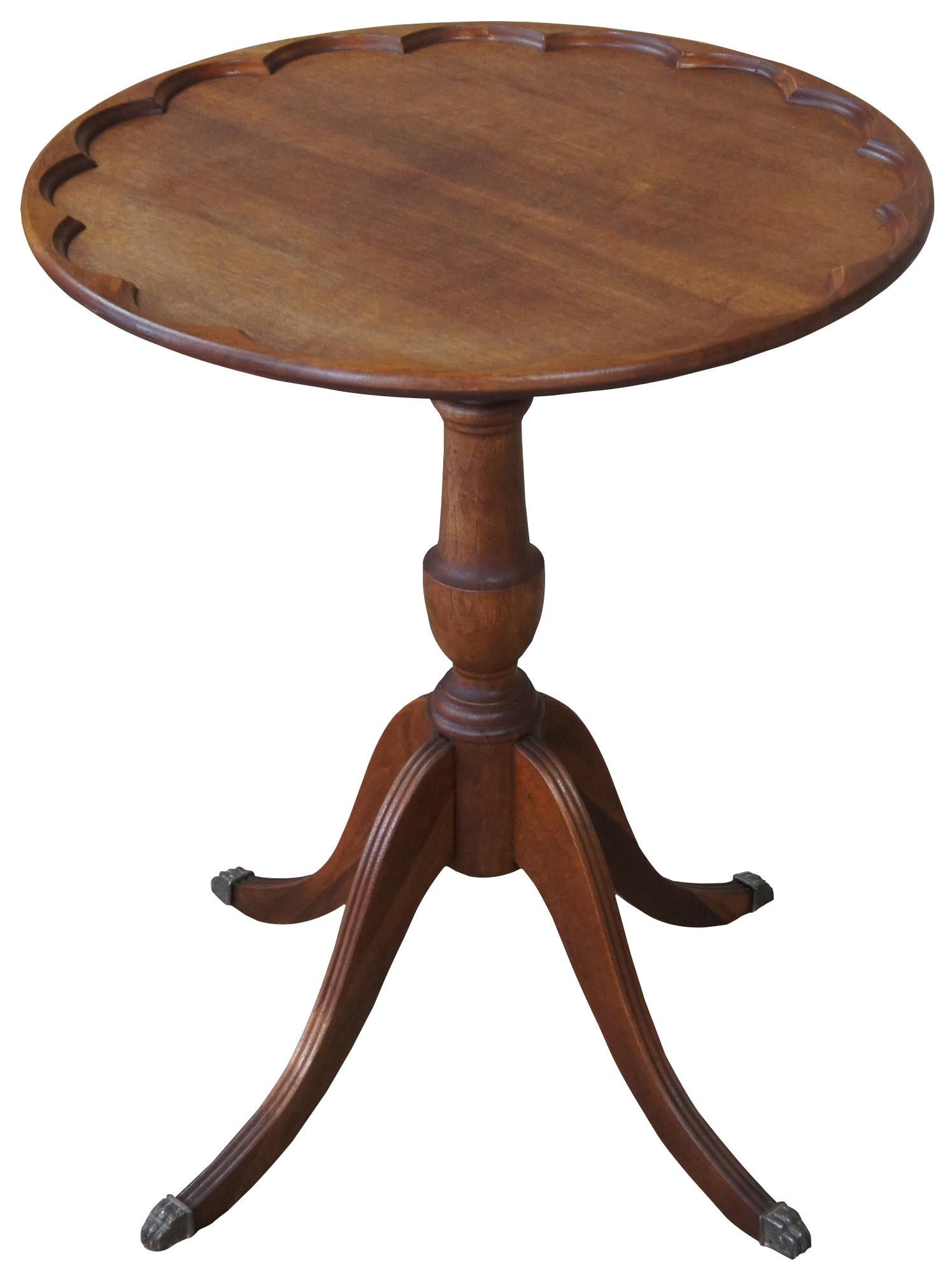 Circa 1940s Duncan Phyfe pie crust table. Features a round top over a turned trophy shaped base leading to four fluted legs with brass capped paw feet. Measures: Feet 22
