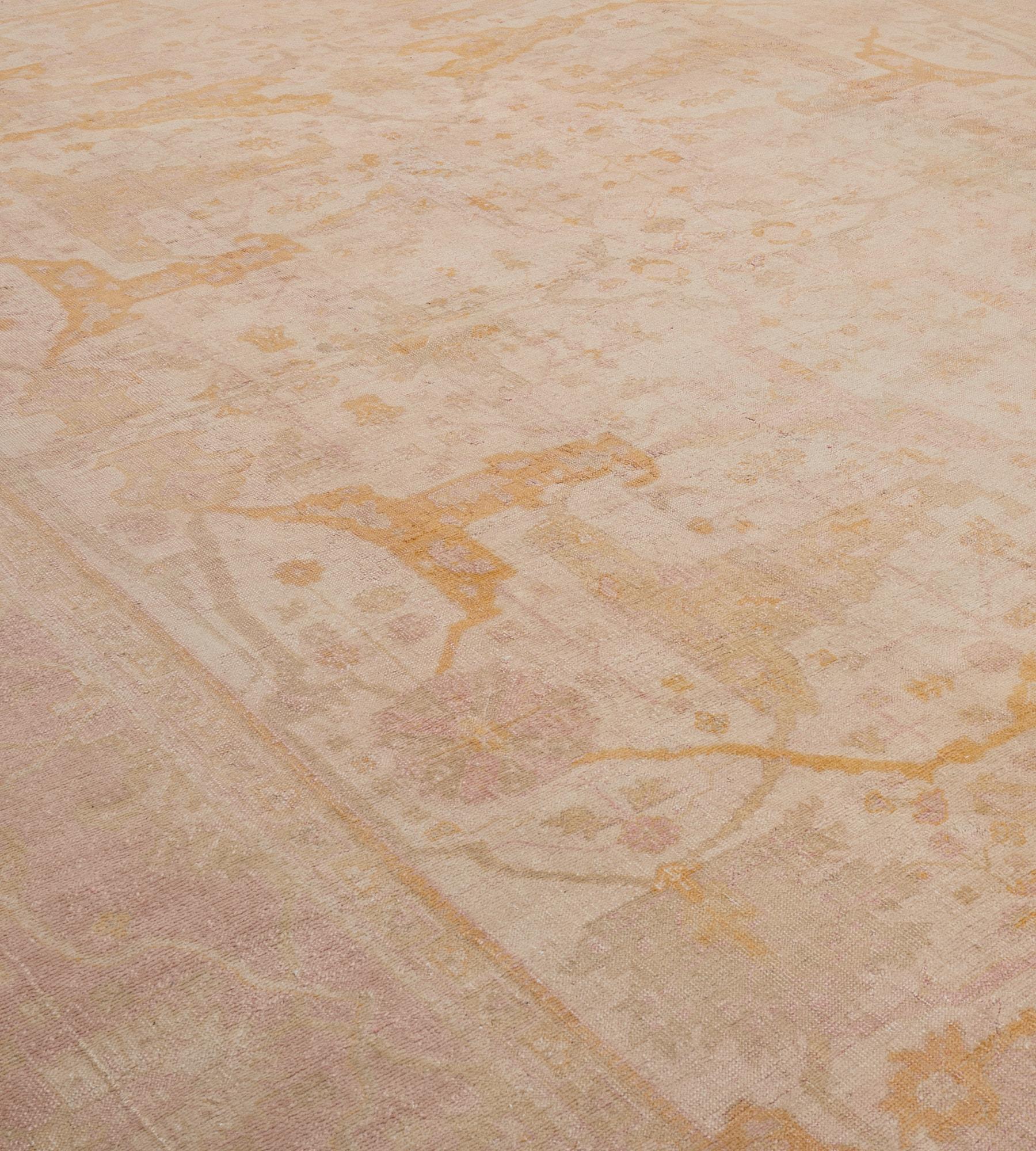 This antique Oushak rug has an ivory field with an overall design of caramel-brown and shaded light grey split palmette vine linking bold dusty-pink and light grey palmette and floral vines, in a broad dusty-pink border of meandering vine linking