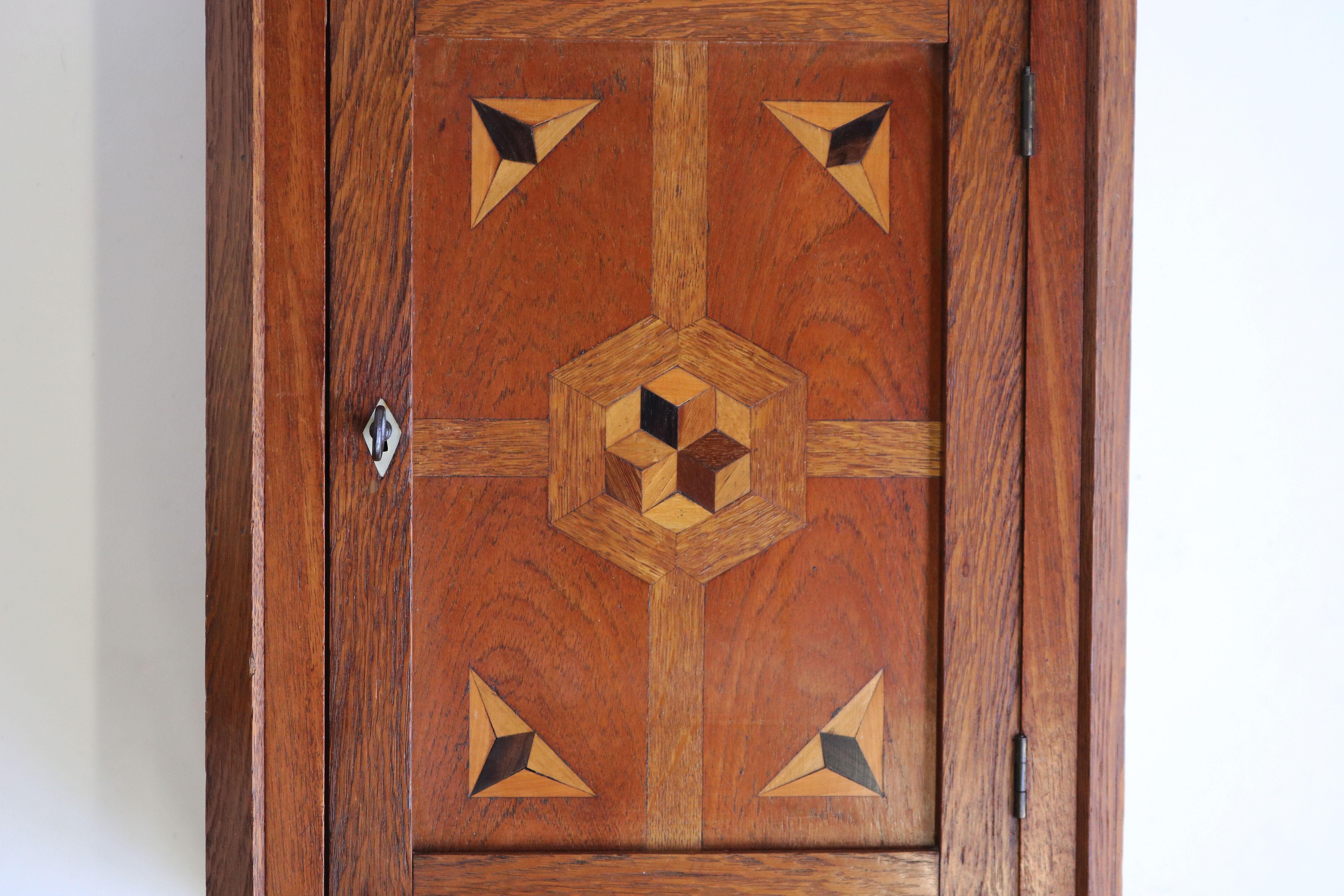 Gorgeous Dutch Art Deco wall cabinet / display cabinet in Amsterdam School design style 1920. 
Made from European oak with various wood inlaid decorations & a mother of pearl key slot. 
A very nice display of craftsmanship & clean Amsterdam School