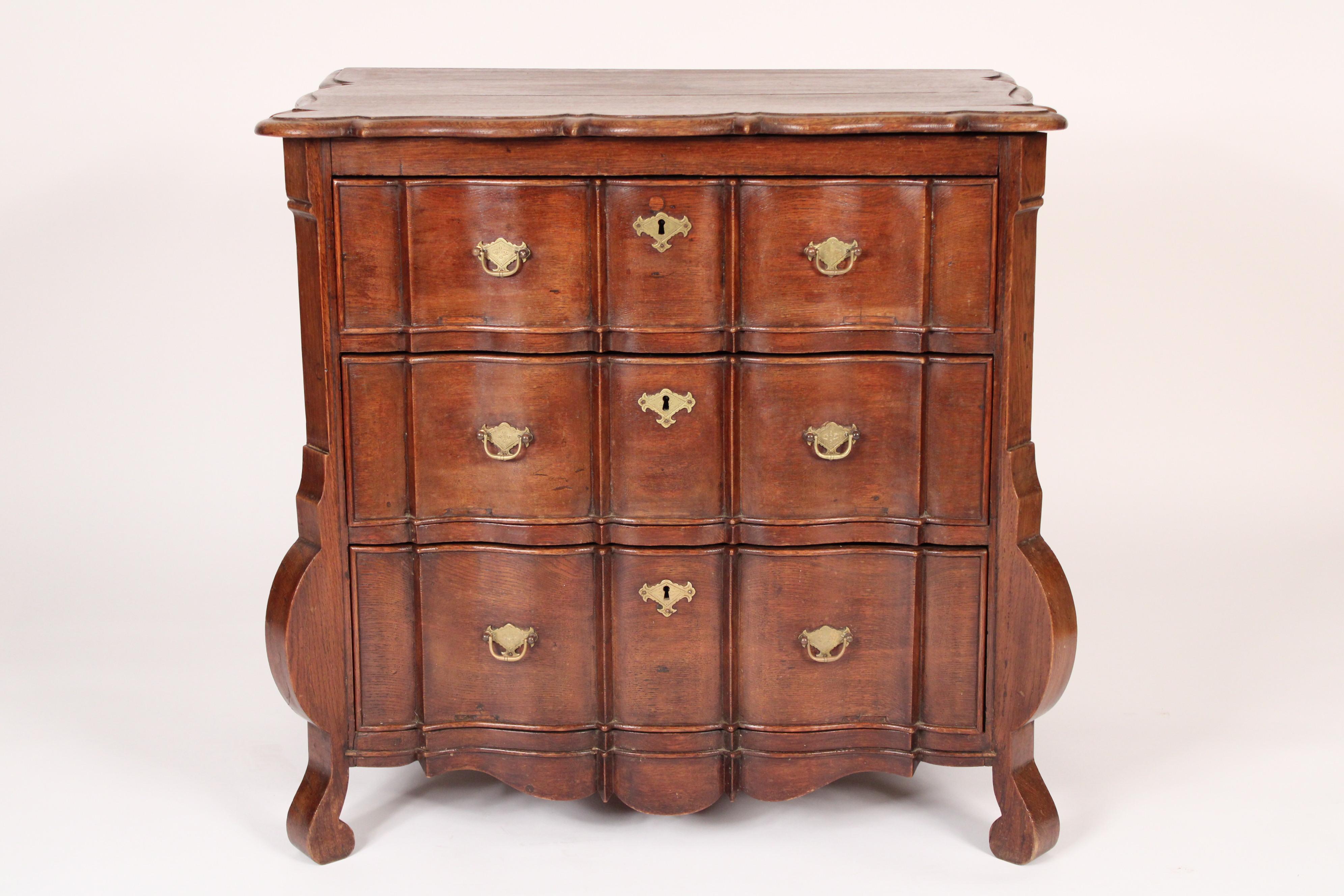 Antique baroque style oak chest of drawers, 19th century. With an overhanging scalloped edge top, three shaped drawers with brass hardware, on scroll shaped feet.