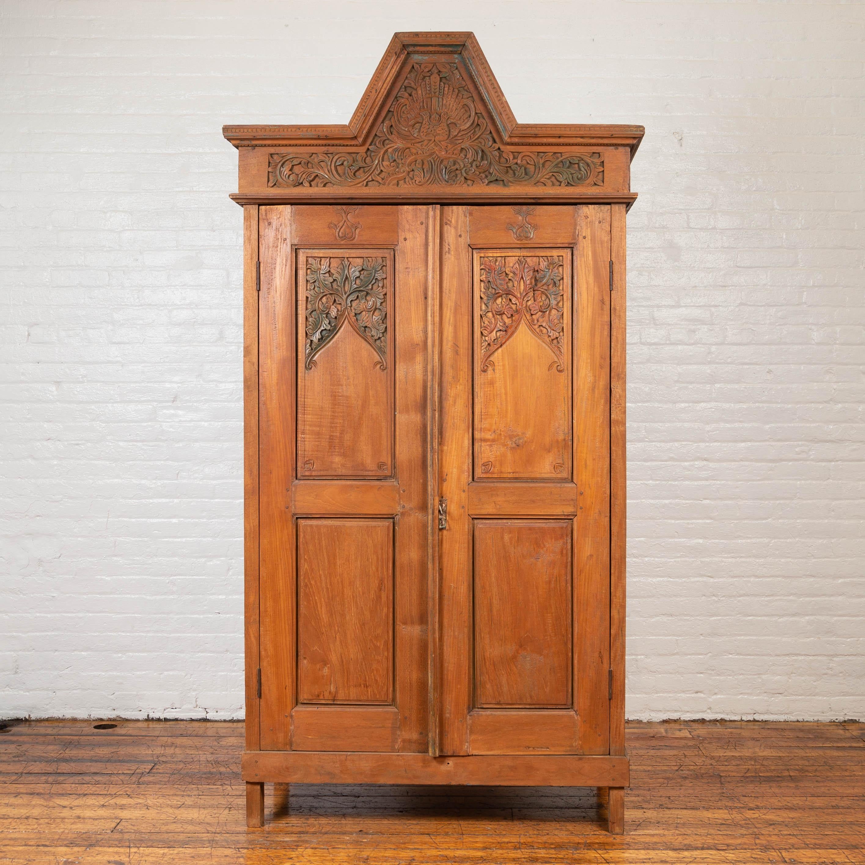 An antique Dutch Colonial armoire from the early 20th century, with low-relief carved birds and foliage. Our eye is immediately drawn to the large cornice will dentil molding that sits atop this armoire, presenting a pyramidal effect surrounding