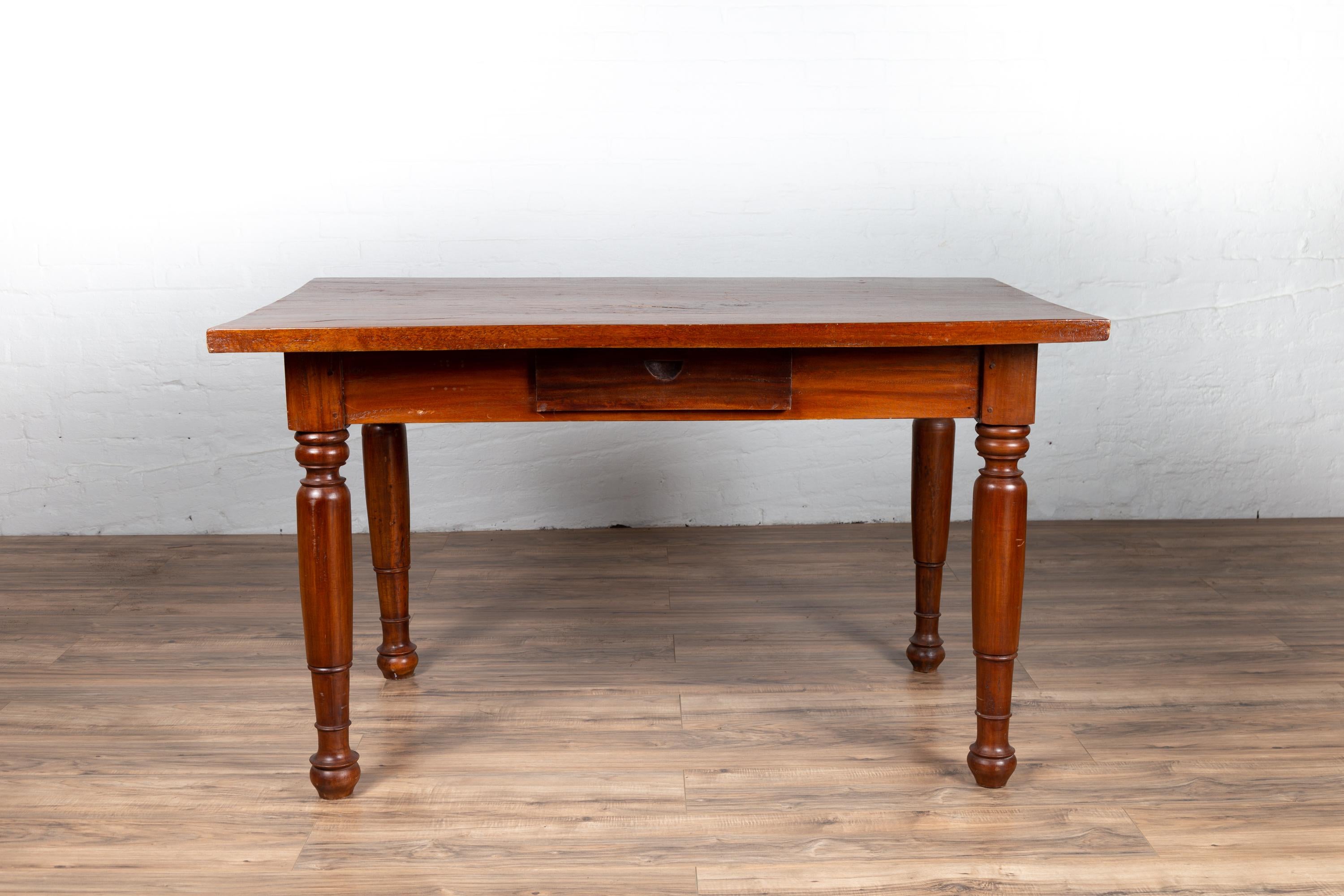 An antique Dutch Colonial Javanese teak desk from the early 20th century, with single drawer and turned legs. Born on the Island of Java in the early years of the 20th century, this Dutch Colonial desk features a rectangular top sitting above an