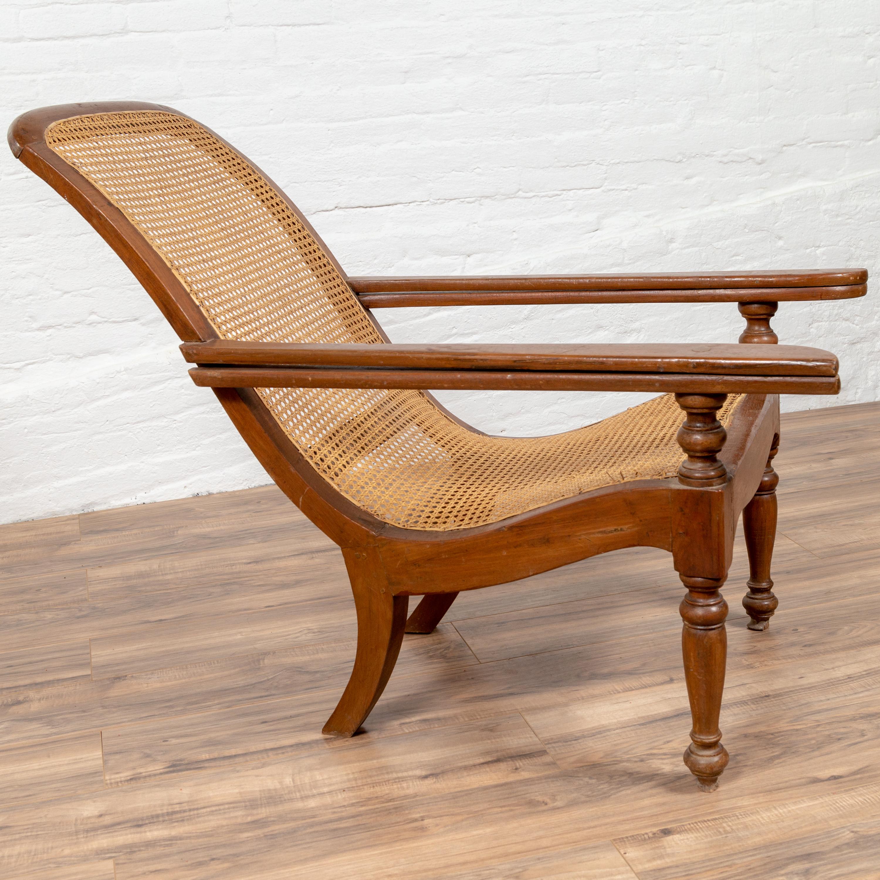 An antique Dutch Colonial Indonesian plantation lounge chair from the early 20th century, with rattan seat and extending arms. Designed to provide a relaxing experience to the sitter, this Dutch Colonial lounge chair features a nicely curving body
