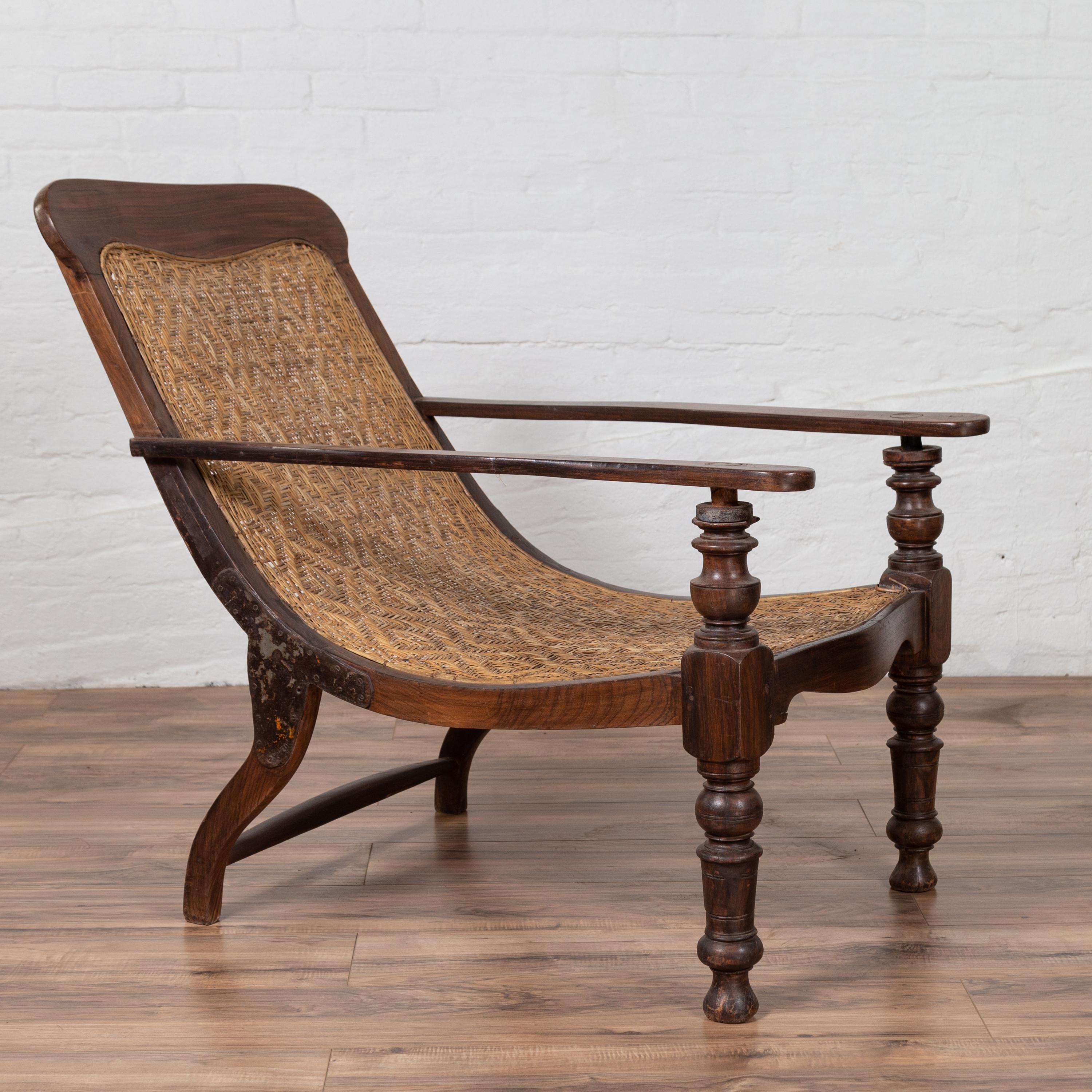 A Dutch Colonial antique Indonesian wooden plantation lounge chair with curving seat and woven rattan accents. Designed to provide a relaxing experience to the sitter, this Dutch Colonial lounge chair features a nicely curving body with rattan seat
