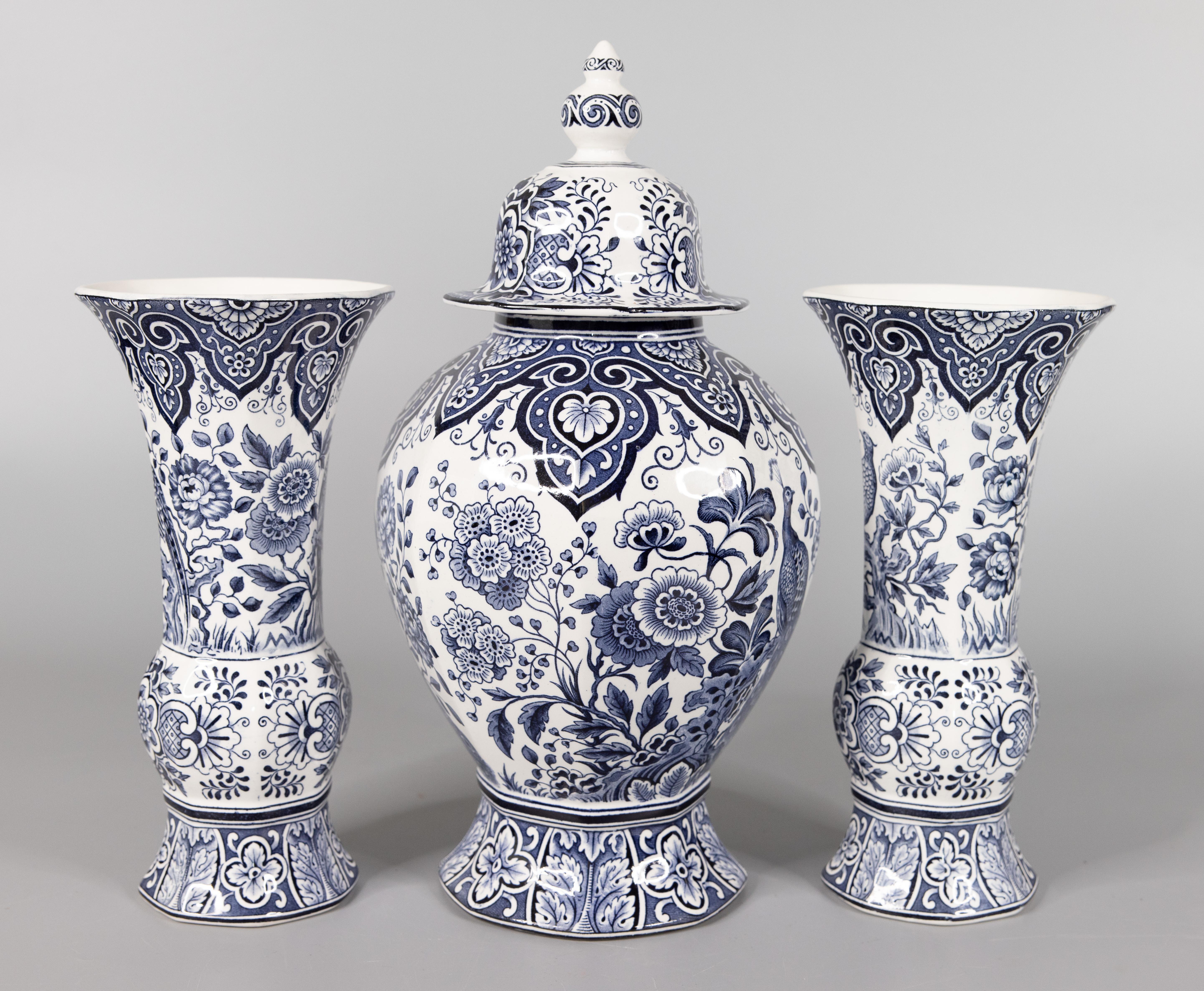 A gorgeous set of three antique Delft garniture vases by Maestricht, made in Holland, circa 1920. Maker's mark on reverse. This fine garniture set has two lovely trumpet vases and one lidded center vase or ginger jar with a peacock and floral