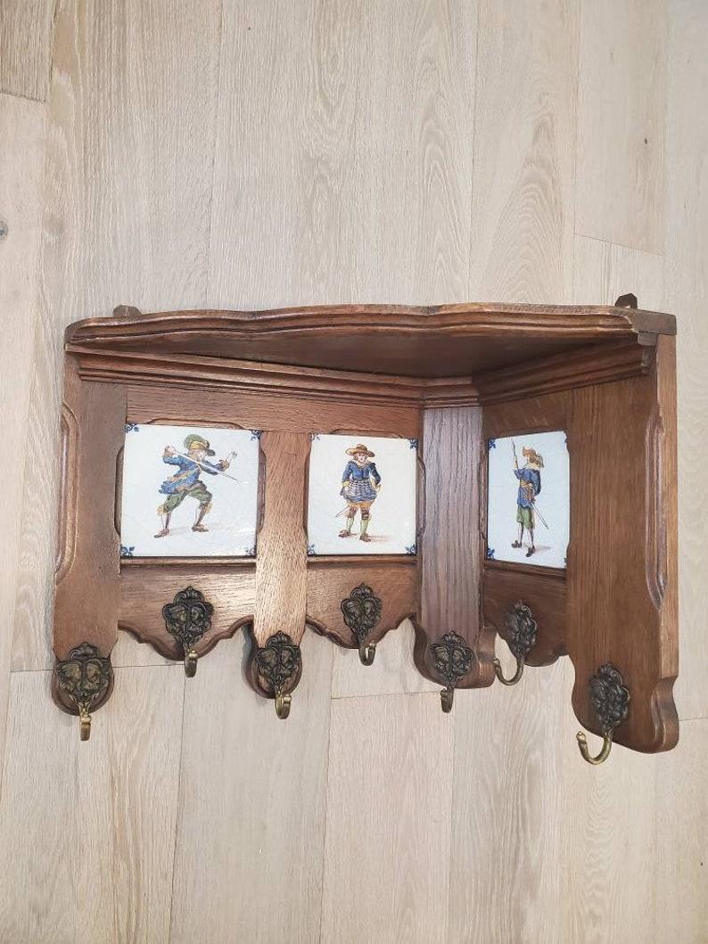 A charming antique wall hanging oak corner shelf coat and hat hanger rack, decorated with three inset original 18th century Dutch Delft tiles, the glazed pottery square tiles feature polychrome painted portraits depicting musketeers, elegantly aged