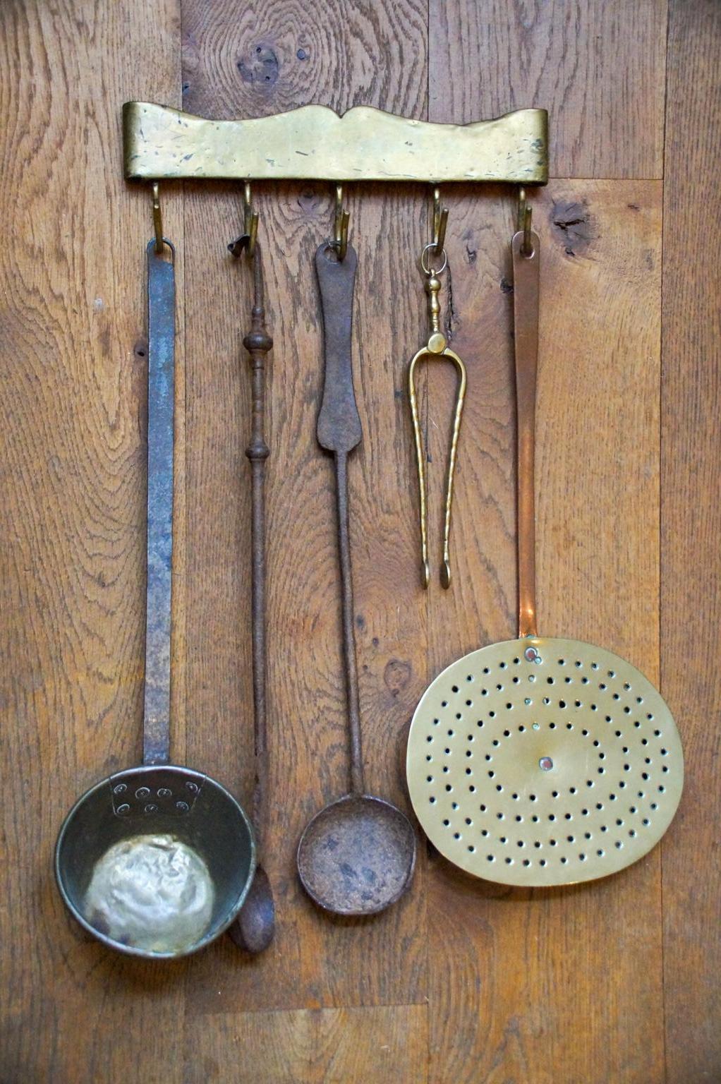 niederländisches Kaminbesteck im Stil Louis XV aus dem 18. bis 19. Jahrhundert, bestehend aus einem Aufhänger und fünf Feuereisen und Küchengeräten. Von links nach rechts sind eine Messingkelle mit schmiedeeisernem Griff, ein schmiedeeiserner