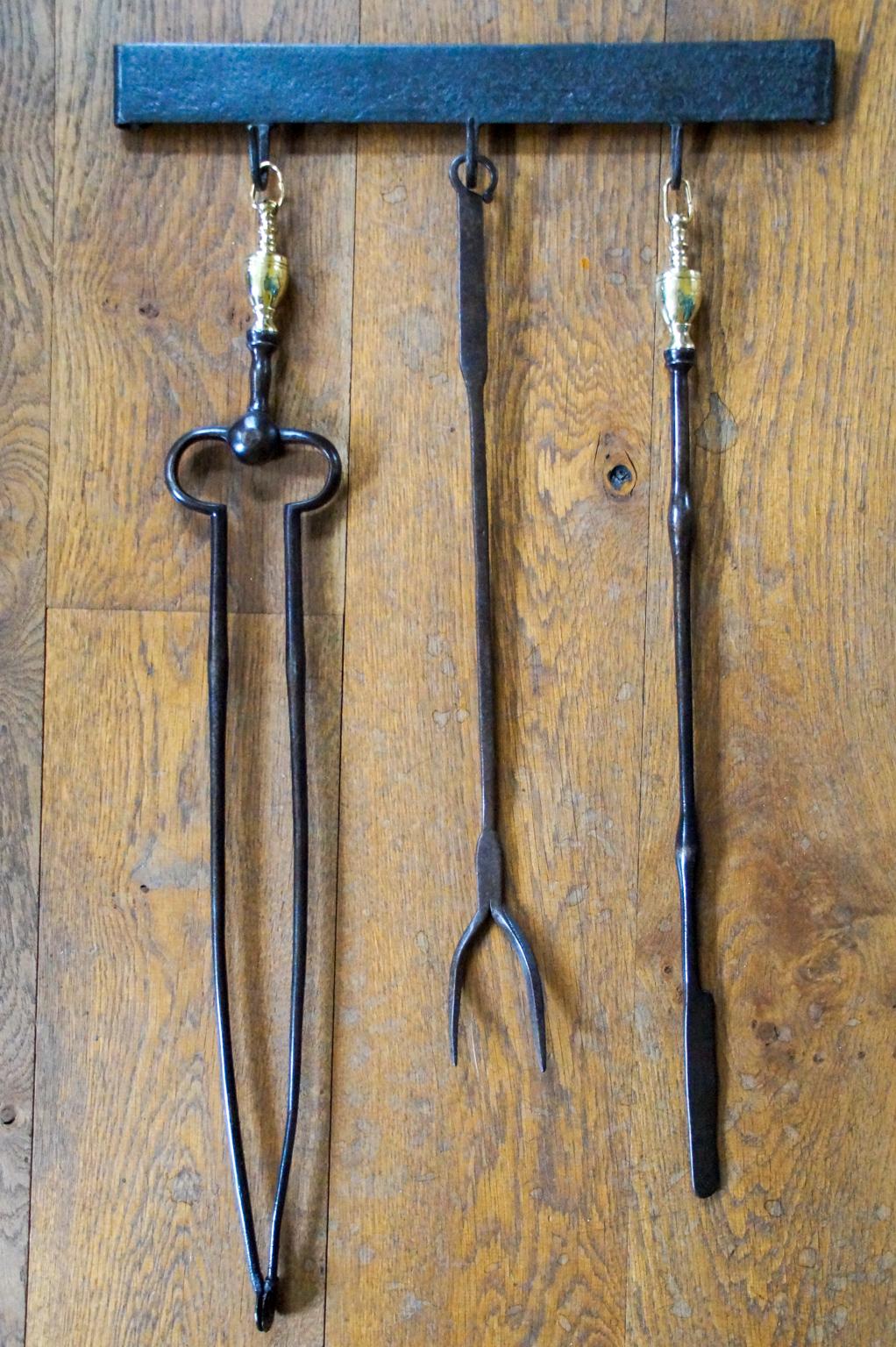 18th - 19th century Dutch Louis XV fireplace tool set consisting of fireplace tongs, a tasting fork, a poker and their hanger. The fire irons are made of wrought iron and the tongs and poker have polished brass handles. The hanger is also made of
