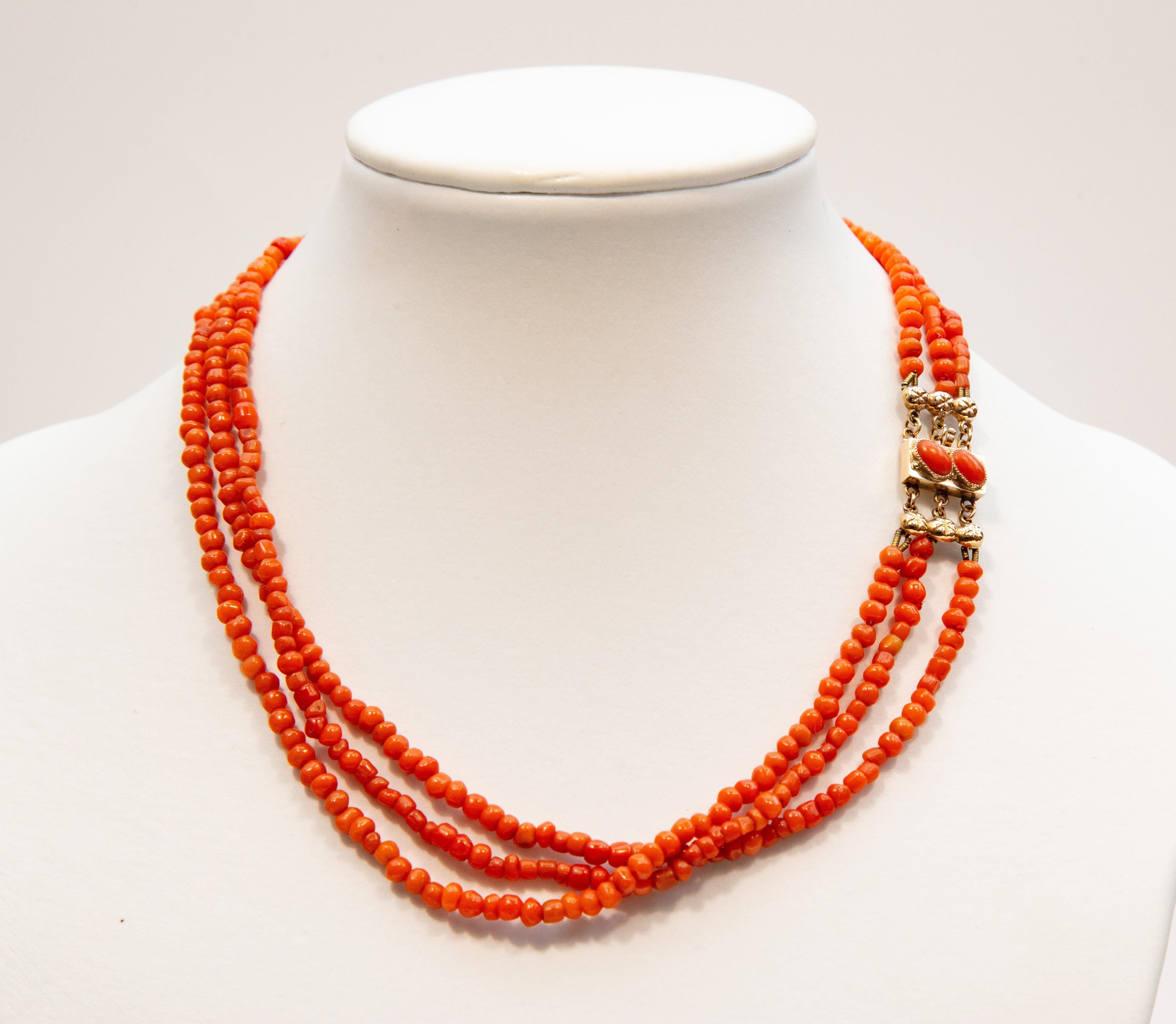 An antique necklace made of 3 strands with red coral beads. The beads of approximately Ø 4 mm are strung on rope. The necklace clasp is made of 14 karat  (585/1000) yellow gold  and is set with 2 cabochon-cut red corals. The clasp is stamped with