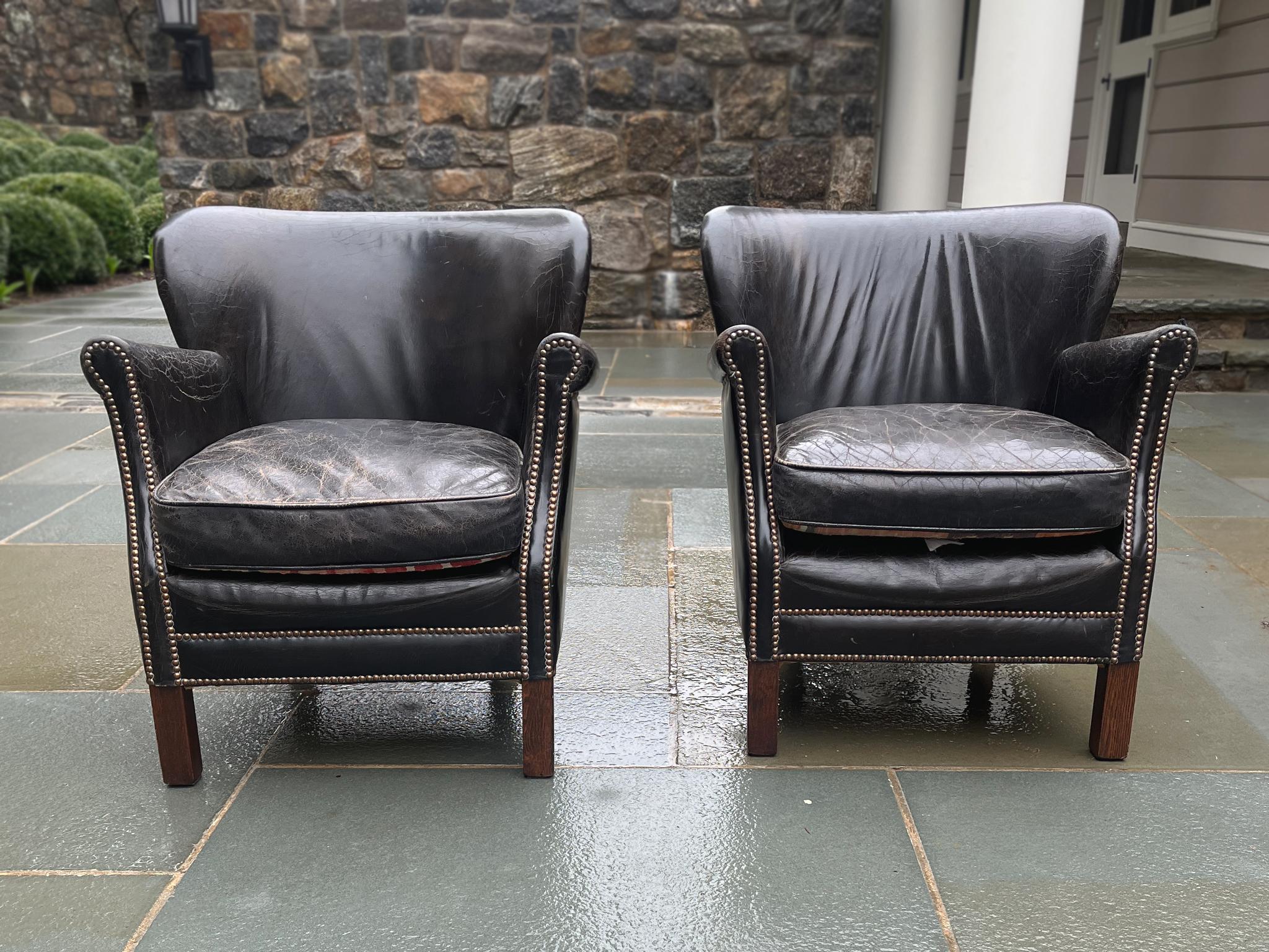 Crafted in the Netherlands in the Early 20th Century, these two club chairs consist of a deep brown leather upholstery with brass trims and dark hardwood legs. The leather has an inimitable lived texture, having aged beautifully over the years and