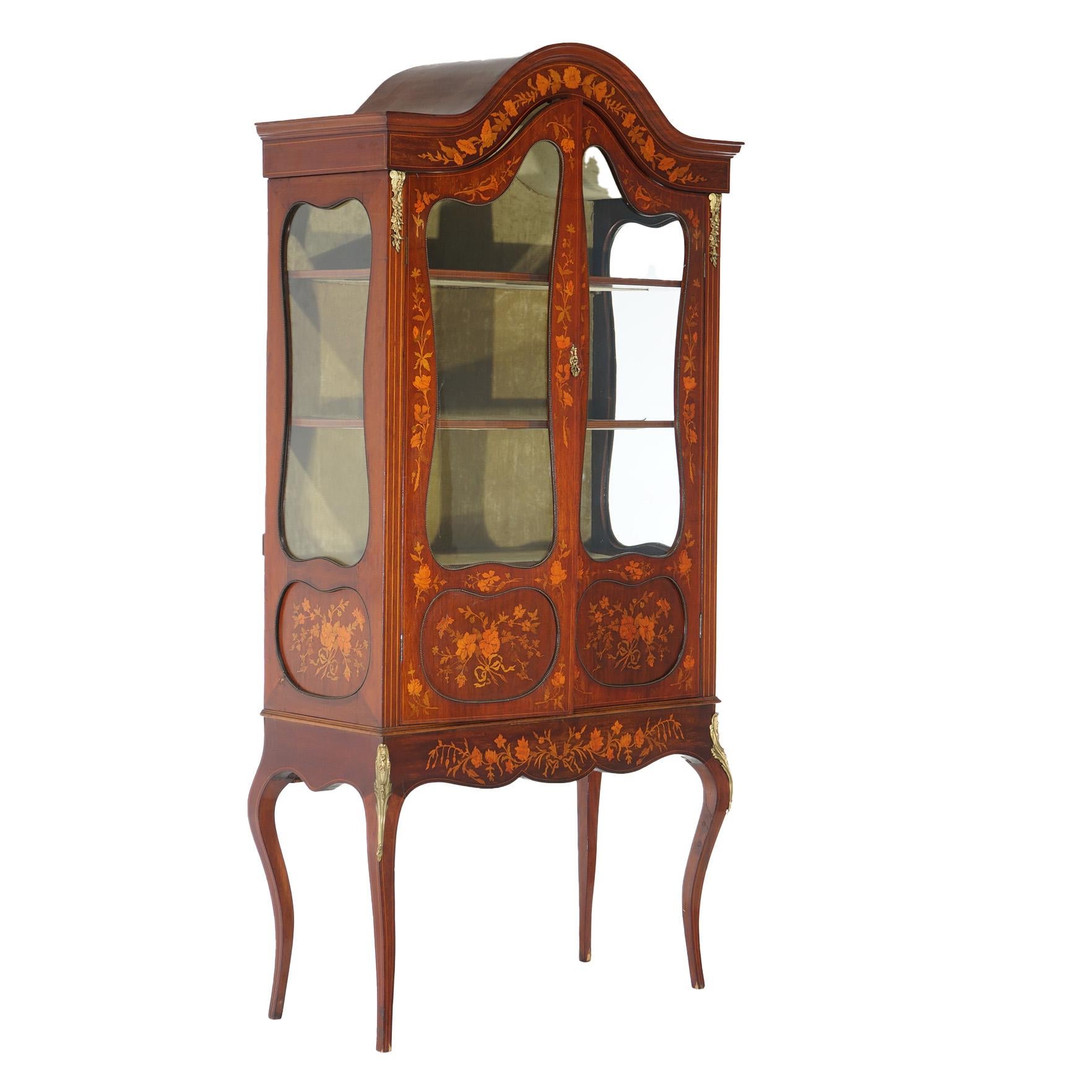 An antique Dutch marquetry display curio cabinet offers mahogany construction with arched form with double glass doors opening to shelved interior, satinwood inlay in floral design throughout, ormolu mounts and raised on cabriole legs,