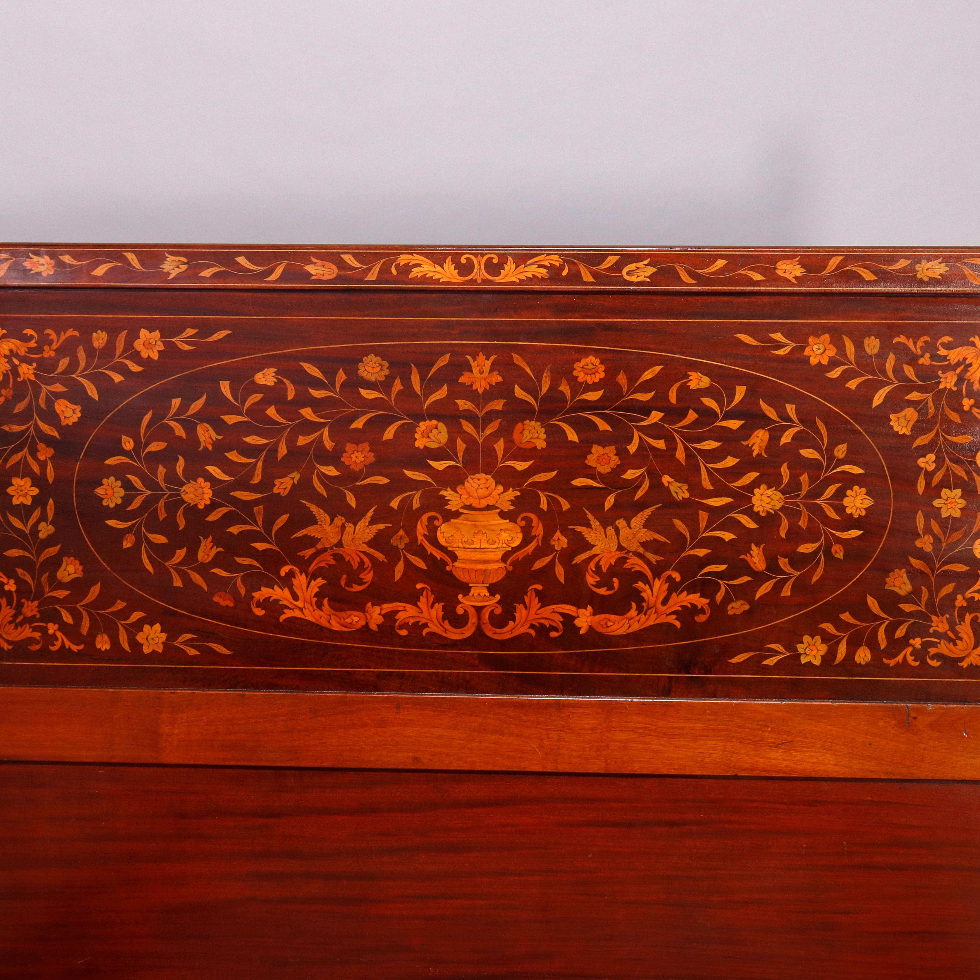 An antique Dutch Marquetry full size bed offers mahogany construction with headboard and footboard having intricately inlaid satinwood urn, floral, foliate and scroll decoration and checked ebonized banding, raised on squared and tapered legs, circa