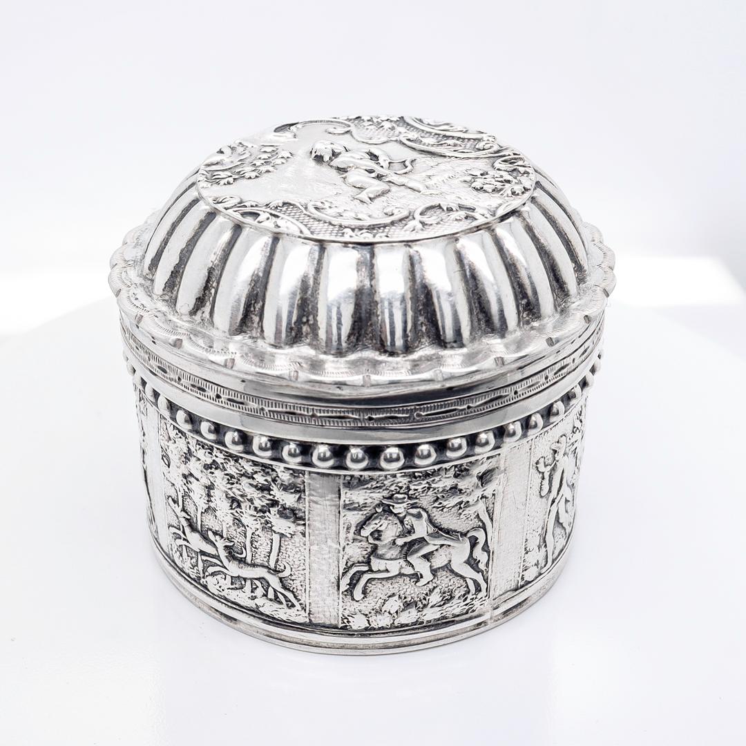 A fine antique, small-scale Dutch round dresser box.

In 833 silver.

With a conforming, hinged lid and a repoussé deer hunt scene to the body and a cupid depiction to the cover.

Marked with Dutch hallmarks to the base and body.

Simply a wonderful