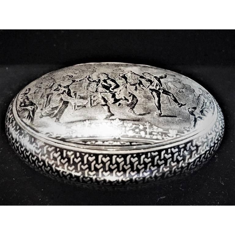 Presented here is an early 19th century Dutch silver snuffbox (circa 1825) of an oval form. The stand-away hinged oval cover is beautifully decorated with black niello enamel, depicting a tavern scene, with peasants dancing and having a great time.