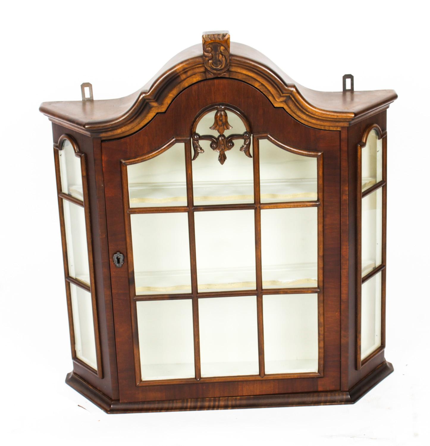 This is an antique Dutch walnut wall hanging cabinet, circa 1840 in date.

The cabinet has canted corners, an arched astragal glazed door and two shelves to display your collectables. the top is surmounted with an acanthus scroll crfesting.

It