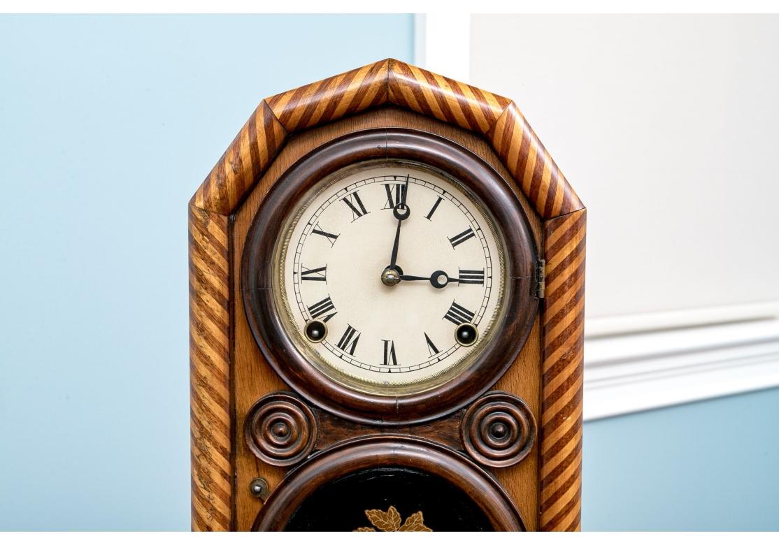 An antique mantel clock by E. Ingraham & Co. with candy stripe inlay, spring driven movement, brass pendulum and key. The clock is patented June 6th, 1871. The door opens to reveal the movement with paper backing. The clock with two conjoined