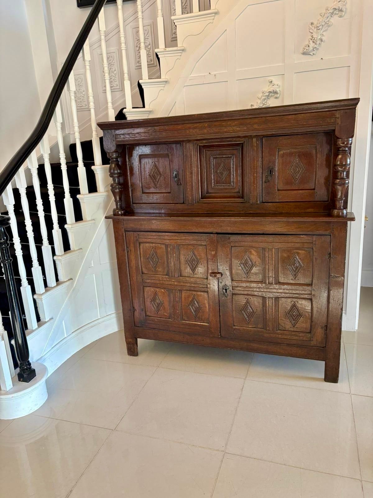 Antique early 17th century original quality oak court cupboard having a moulded cornice above a centre carved oak panel flanked by a pair of carved oak doors with original iron locks and drop handles. The doors open to reveal a storage compartment