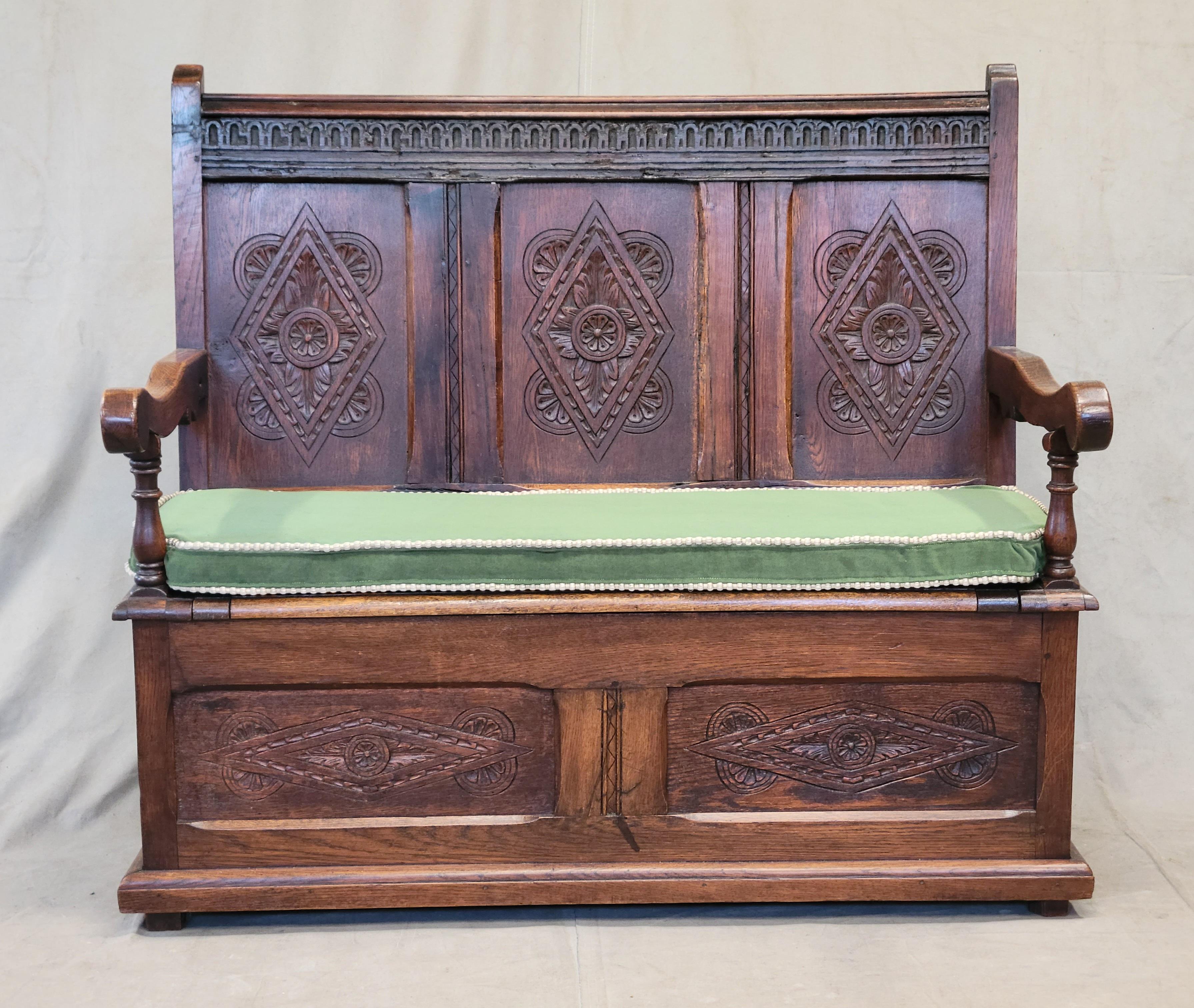 A stunning traditional antique early 1800s Georgian English hand carved dark oak settle storage bench or monk's bench. Beautiful carved arm rests add a decorative element while hand-carved oak panels with a diamond pattern are on the backrest and