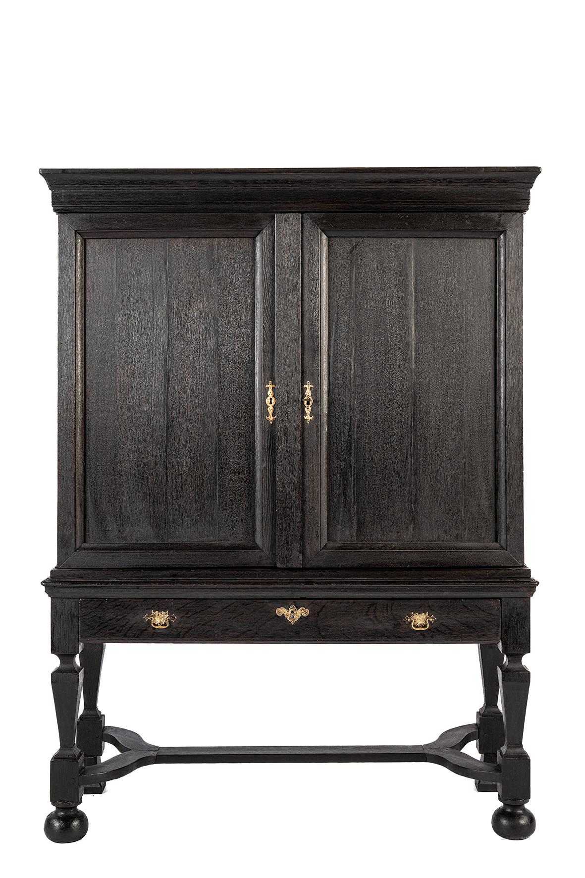 This Dutch table cabinet, also known as a cross-legged cabinet, is made of oak and has a deep, almost black finish, which suggests a traditional treatment such as ebonized stain or dark varnish. The cabinet stands on a distinctive base with four