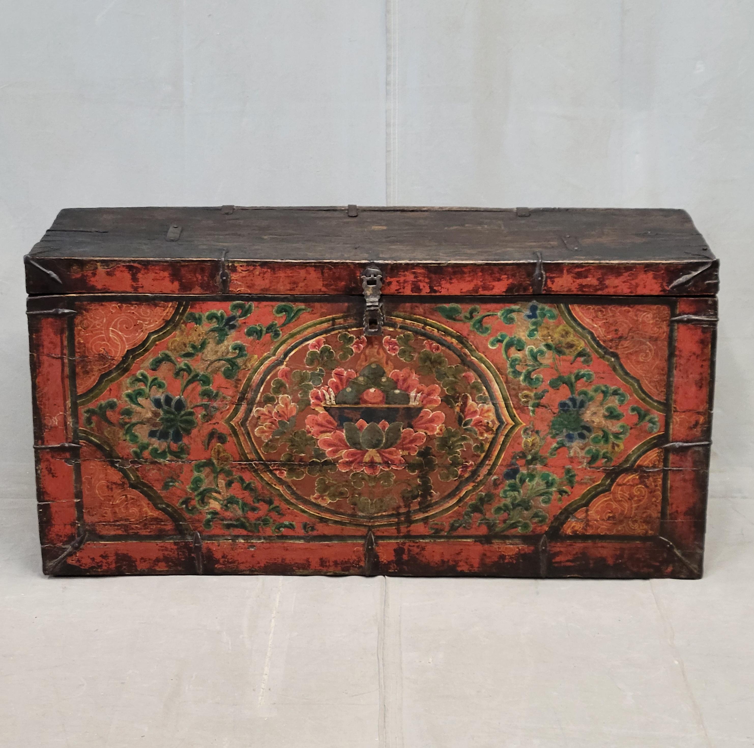 A beautiful antique early 1900s lacquer storage box or trunk from Tibet. The red, blue, green and ochre lacquer on the box front is used to create lotus, floral and flaming jewel motifs. The top of and sides of the box are abraded from age and use.