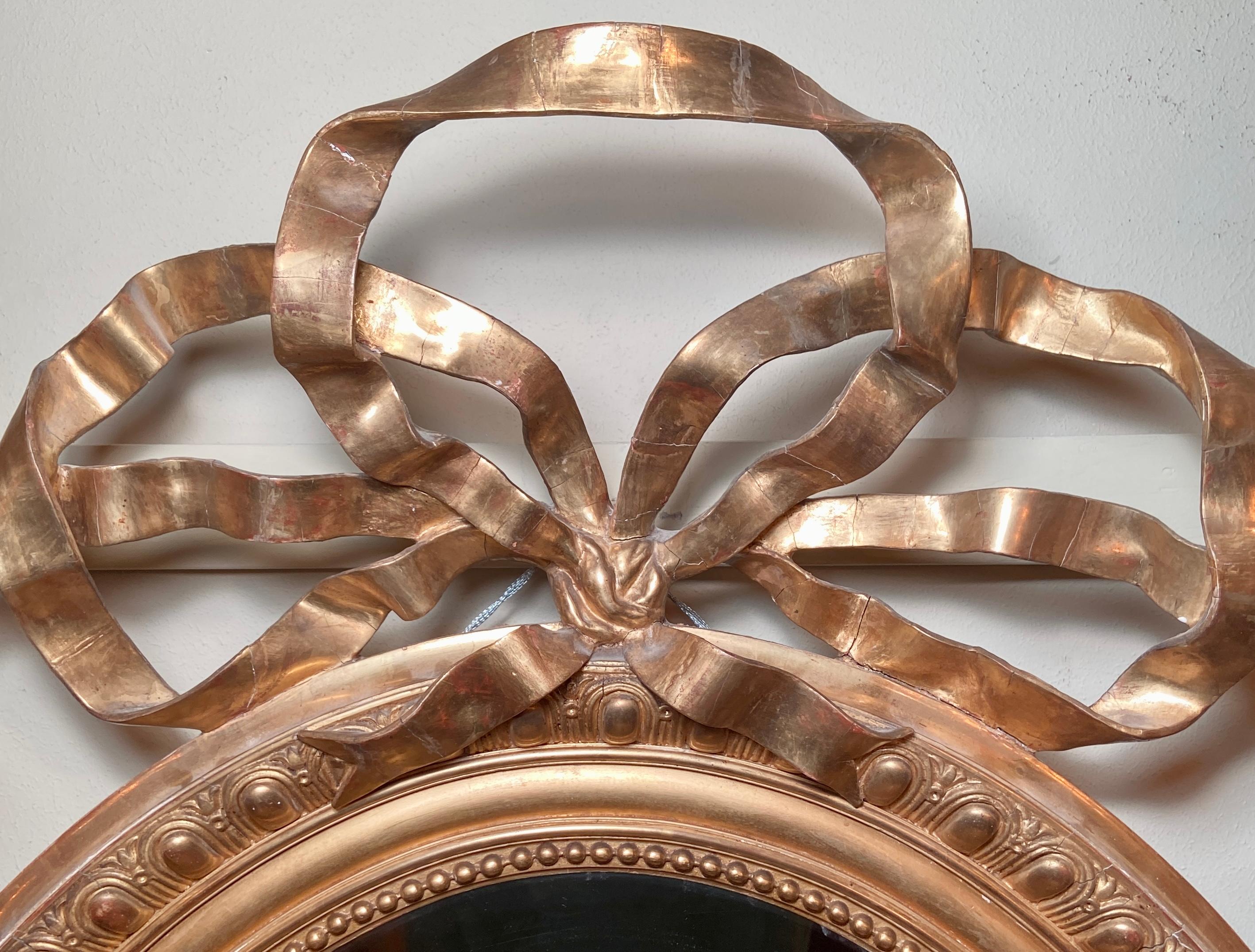 Antique early 19th century French extraordinary gold leaf mirror, oval-shaped with ribbon & bow detail.