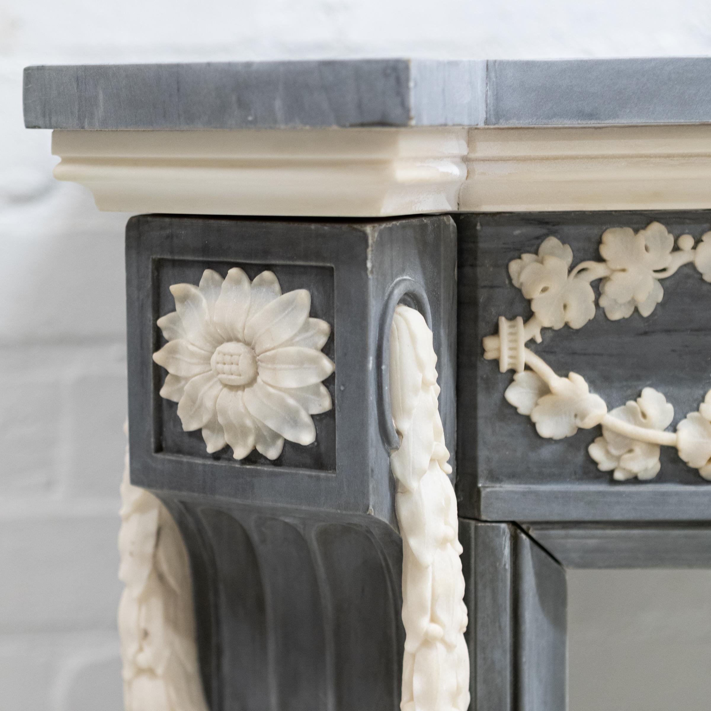 This impressive antique French-style Louis XVI fireplace surround has been expertly carved and crafted from grey marble with delicate statuary marble details to the jambs and frieze.

The well-figured shelf has stepped and canted corners. Each