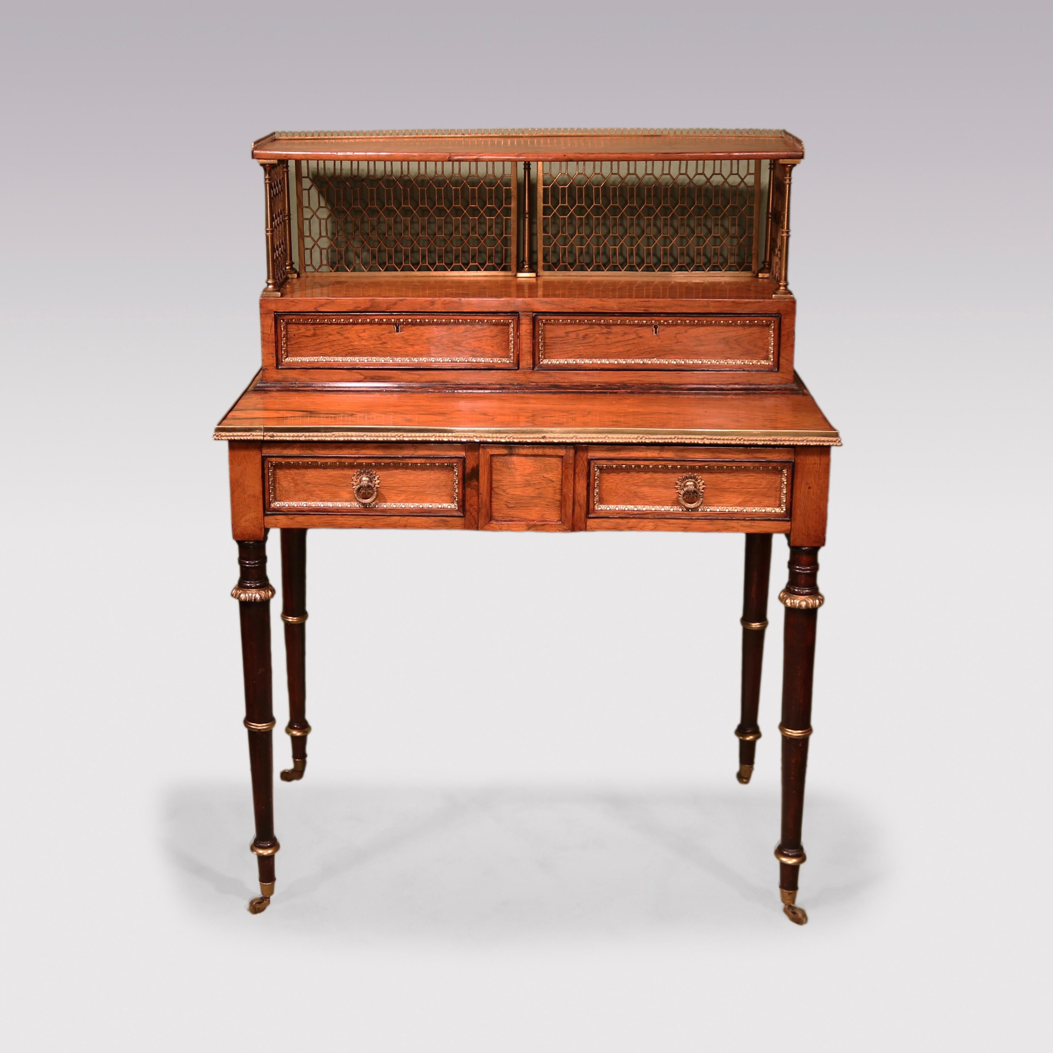 An early 19th century Regency period Rosewood Bonheur du Jour in the style of John McLean having distinctive gilt brass fretwork upper part with two small drawers above brass edged lower section with panelled and brass framed drawer, supported on