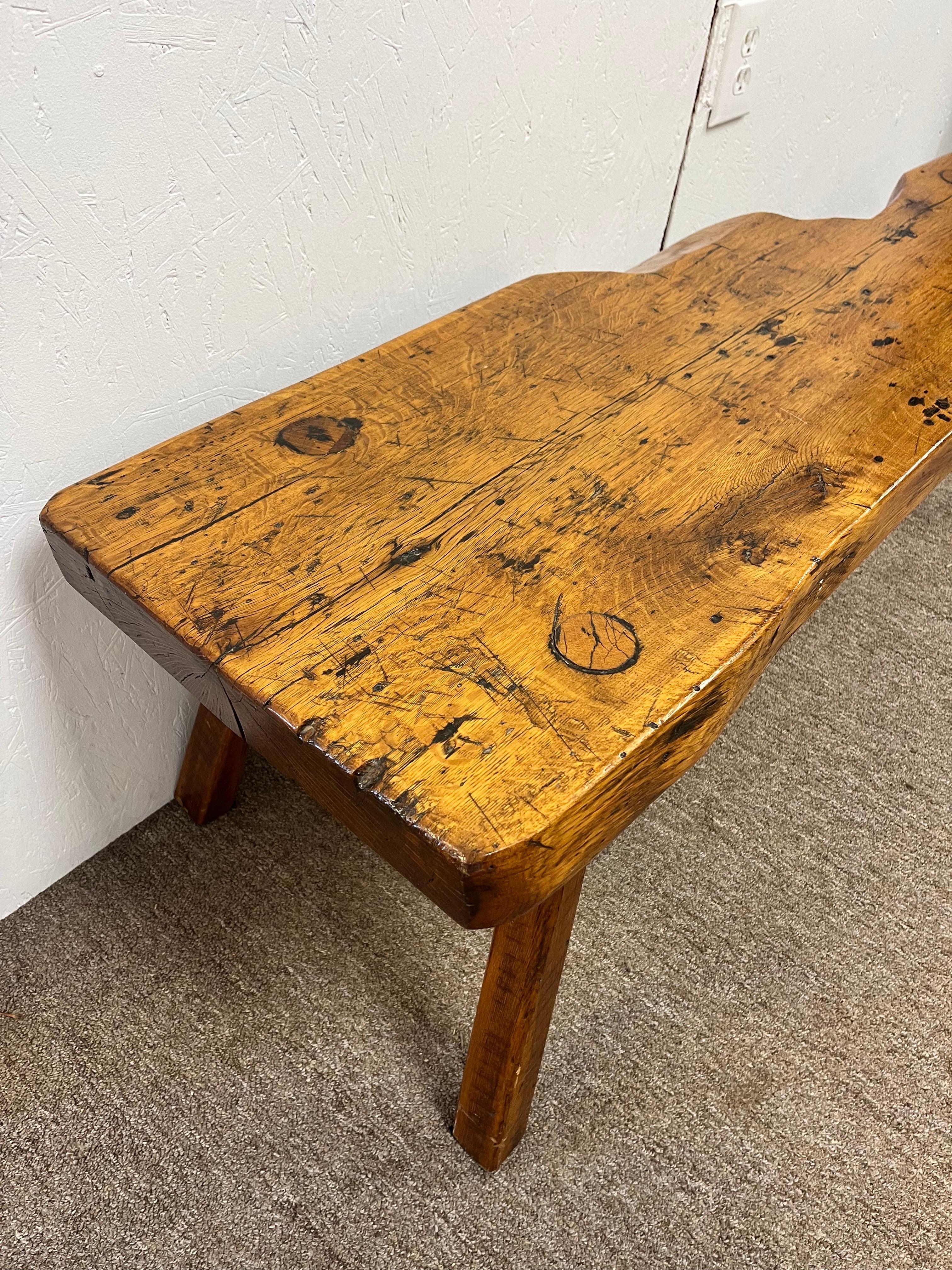An antique early 19th Century circa 1820's rustic bench hand made from a thick, oversized slab of wood with hand carved and joined splayed legs that run through the seat. The bench seat has a fascinating cut out (if you will) that may have been an