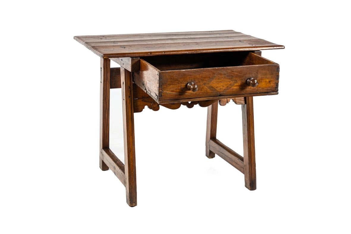 This piece is an antique Spanish side table crafted from pine wood. It has acquired a warm, light honey tone with a deep natural sheen and a rich patina built up over generations of use. The top is constructed from wide boards, and the front is