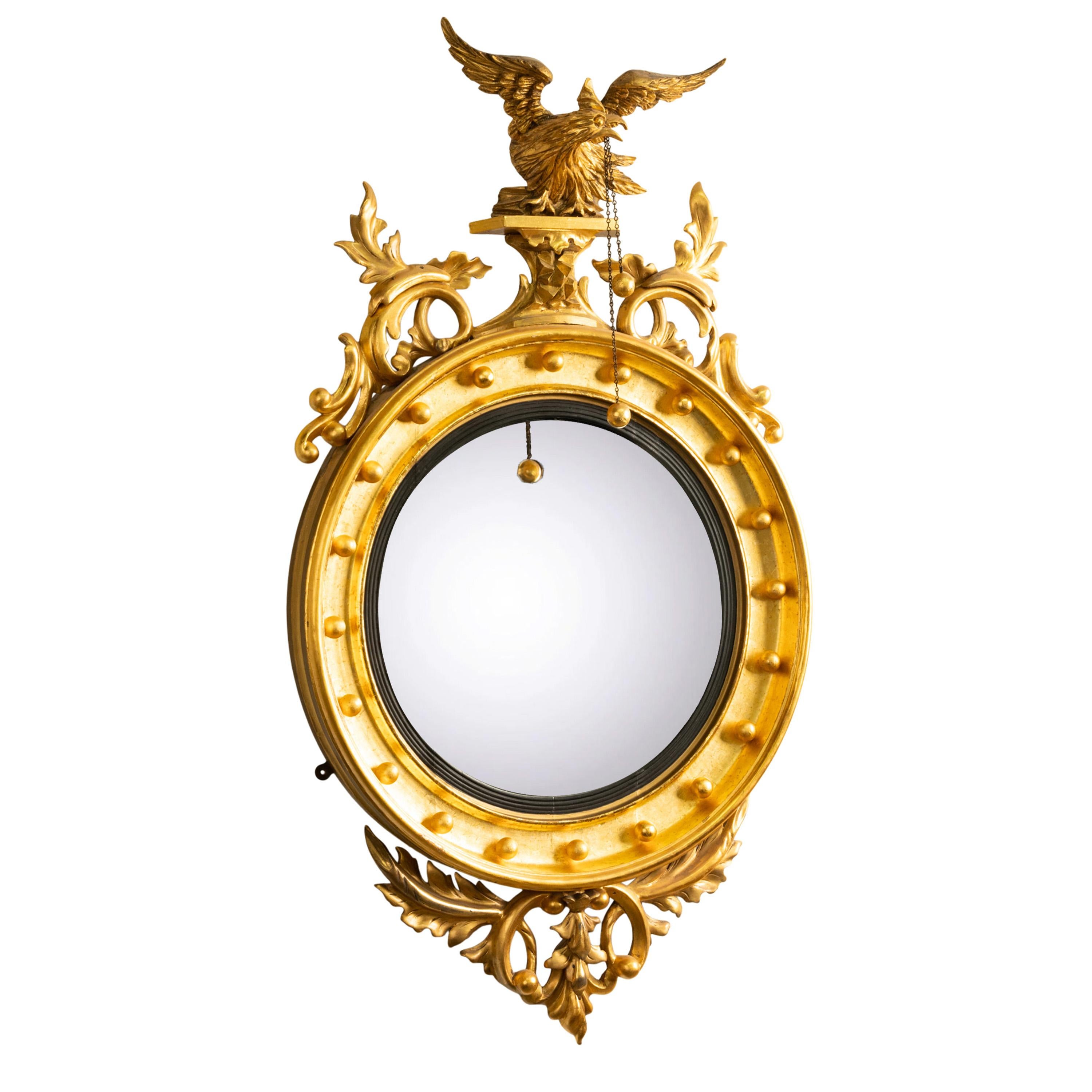 A fine antique American Federal period convex gilt wood looking Glass/ mirror, circa 1820.
The mirror sumounted with a carved eagle on a plinth, the eagle with a chain suspended from it's beak with two gilt spheres, the eagle is flanked by stylised