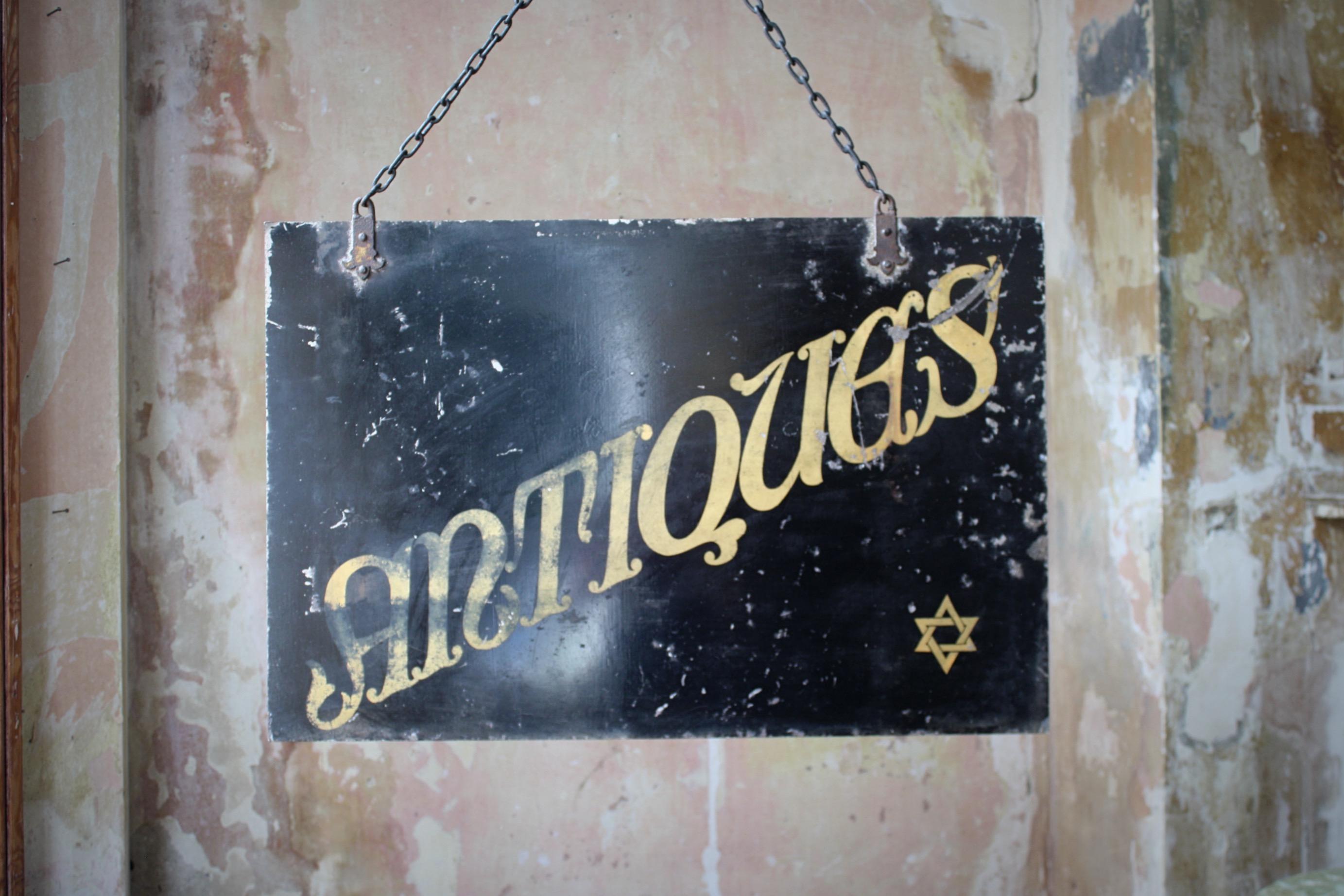 Hanging double sided trade sign, sheet metal with a black ground and gilt lettering. Two pretty cast iron riveted hanging brackets.

A small Star of Solomon is located in the corner of each side, giving the indiction it was previously used to trade
