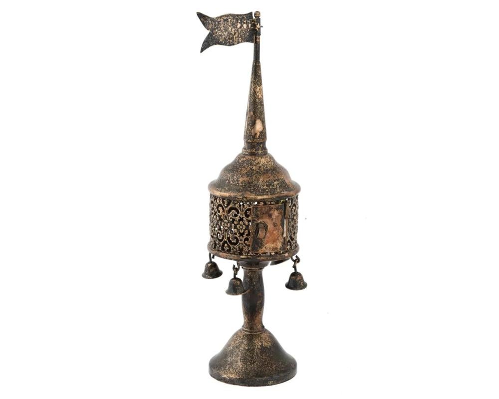 An antique Judaica spice tower or Besamim box made in the early 20th century, crafted in sterling silver with intricate swirling floral openwork designs on the body with dangling bells below. The tapered stem base and the flag on top of the spire