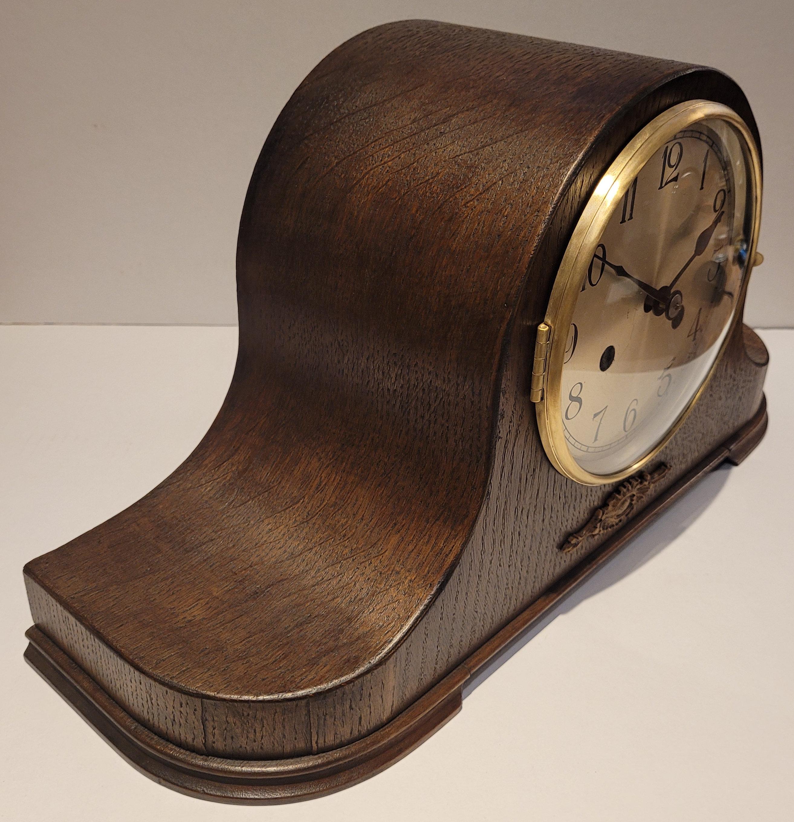 This is an antique early 20th century c1920's German chiming mantel clock. This is in fantastic condition and is in full working order. It has a beautiful Napoleon hat shaped oak body with a carved embellishment below the face. The oak has a dark