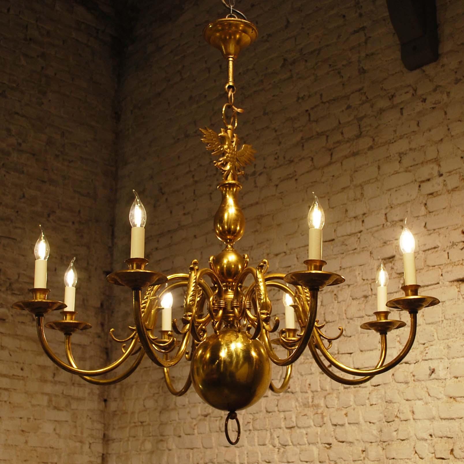 A large eight-light Baroque style brass Dutch chandelier with ball-shaped elements. 
It has eight arms that end in brass bobeches with cardboard candles on top. A bobeche is a bowl on a chandelier, sconce, or candelabra with the historical purpose