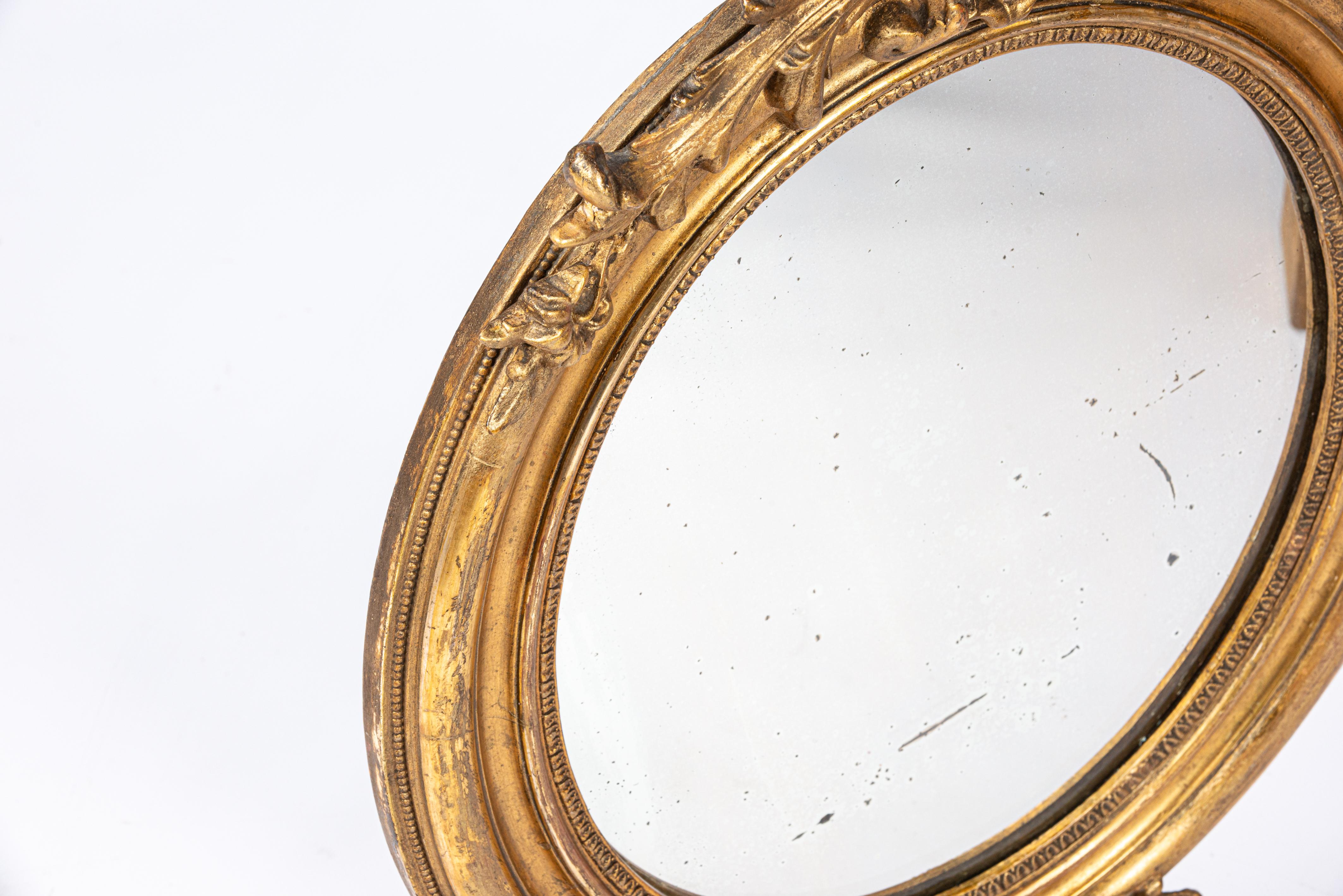 Nous vous proposons ici un magnifique miroir ovale ancien fabriqué dans le nord de la France au début du 20e siècle, vers 1910. Le cadre du miroir a été enrichi d'un ruban à nœuds sur le dessus et d'un perlage qui entoure le verre. Les décorations