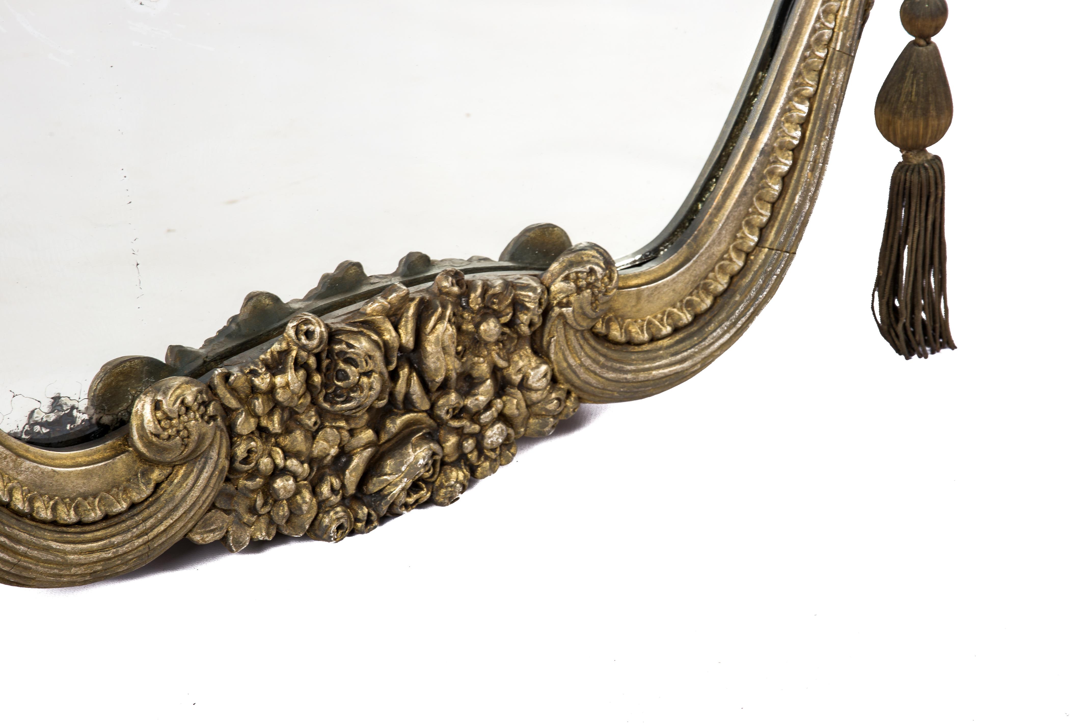 This beautiful and unique mirror was made in central France in the early 20th century, circa 1910. The mirror frame features a central group of flowers flanked by two scrolls. The frame has a solid pine base smoothened with gesso. It has a grey