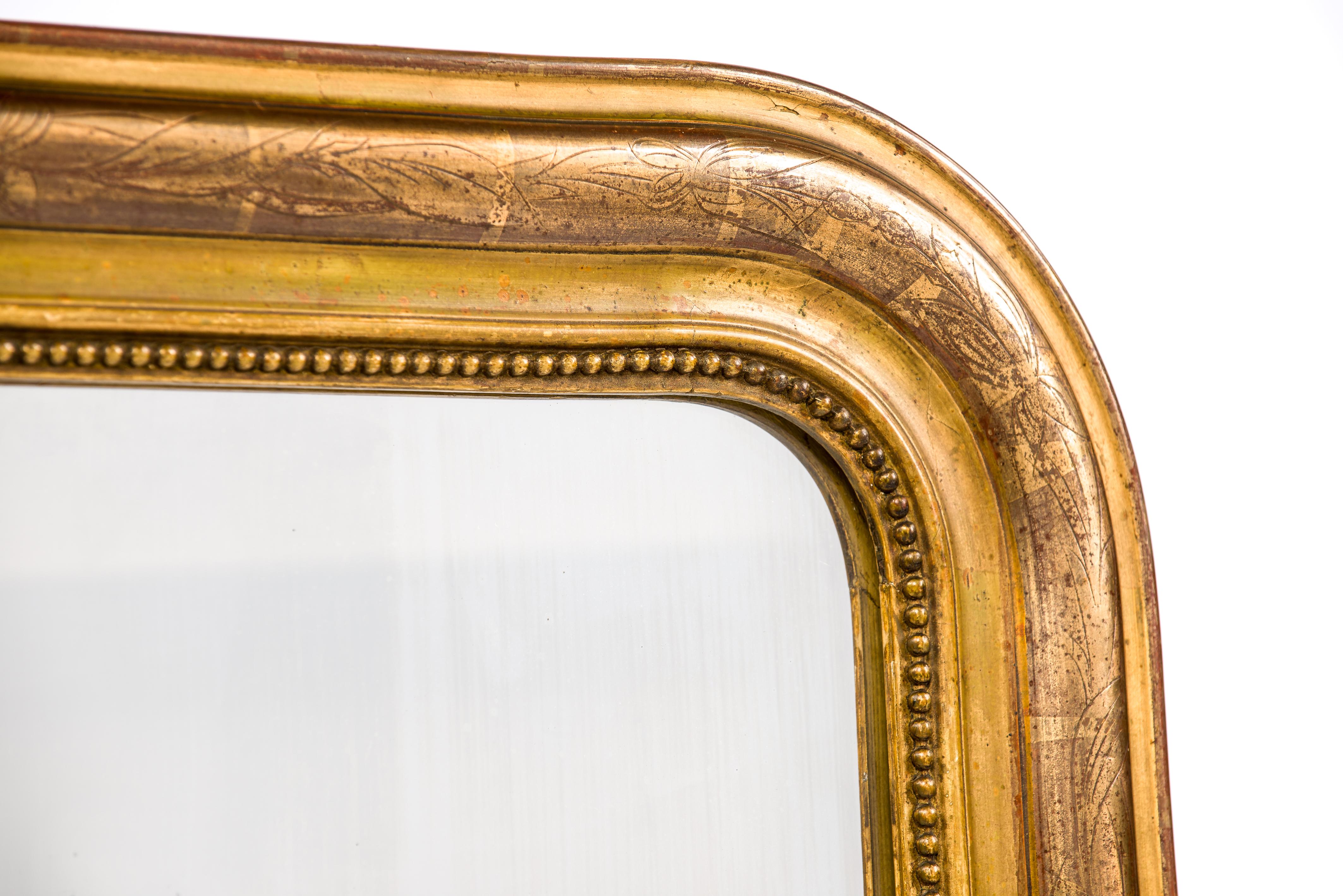This beautiful antique mirror was made in France in august 1903. It features the upper rounded corners typical for the Louis Philippe style. The mirror has a solid pine frame that was smoothened with gesso. The most elevated part was engraved with a