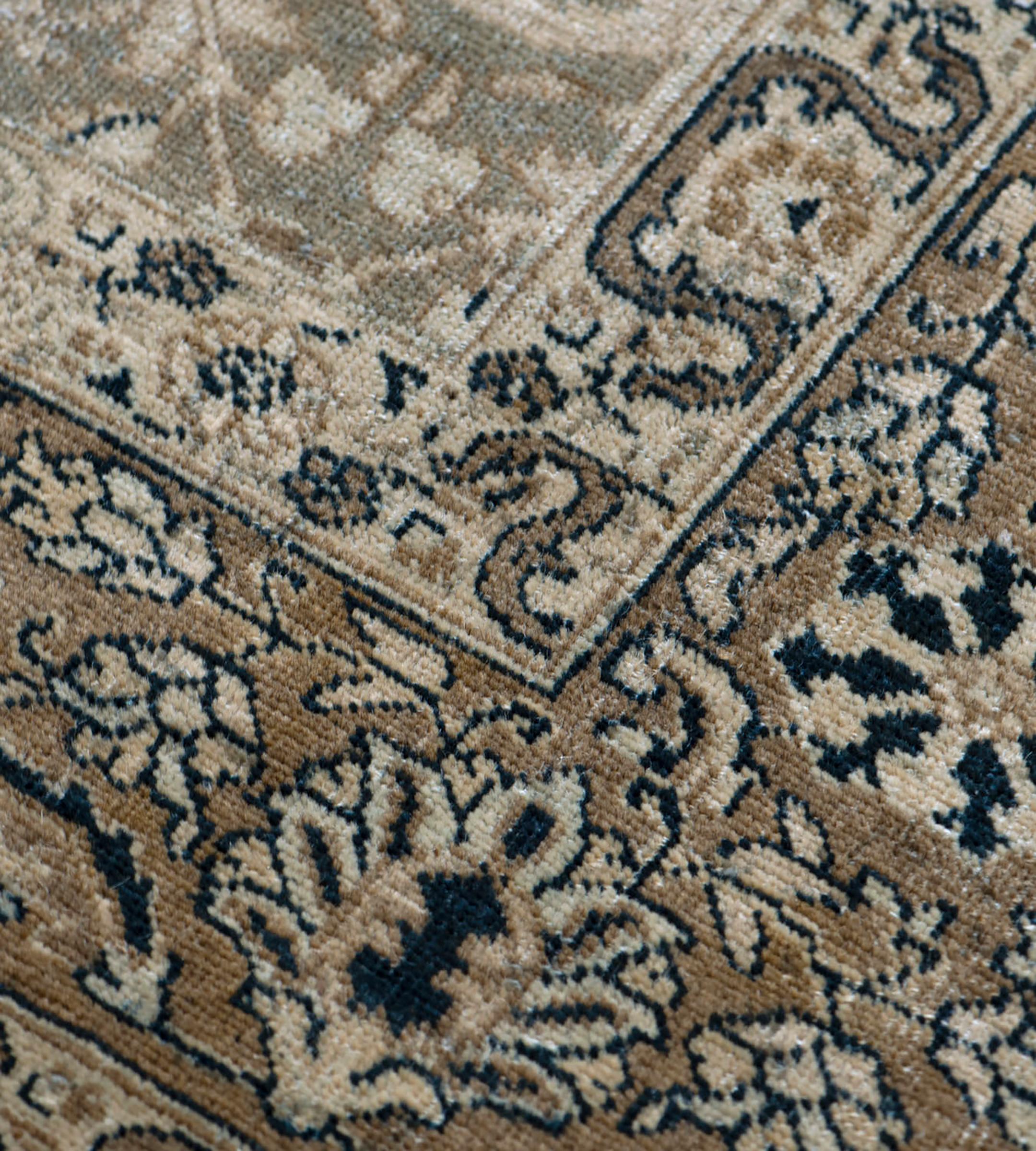 This early 20th Century hand-woven Persian Tabriz rug features a green-grey field with an overall design of sandy-yellow, charcoal-blue and ivory delicate palmette and floral vine, in a buff-brown border of delicate palmette and floral vine between