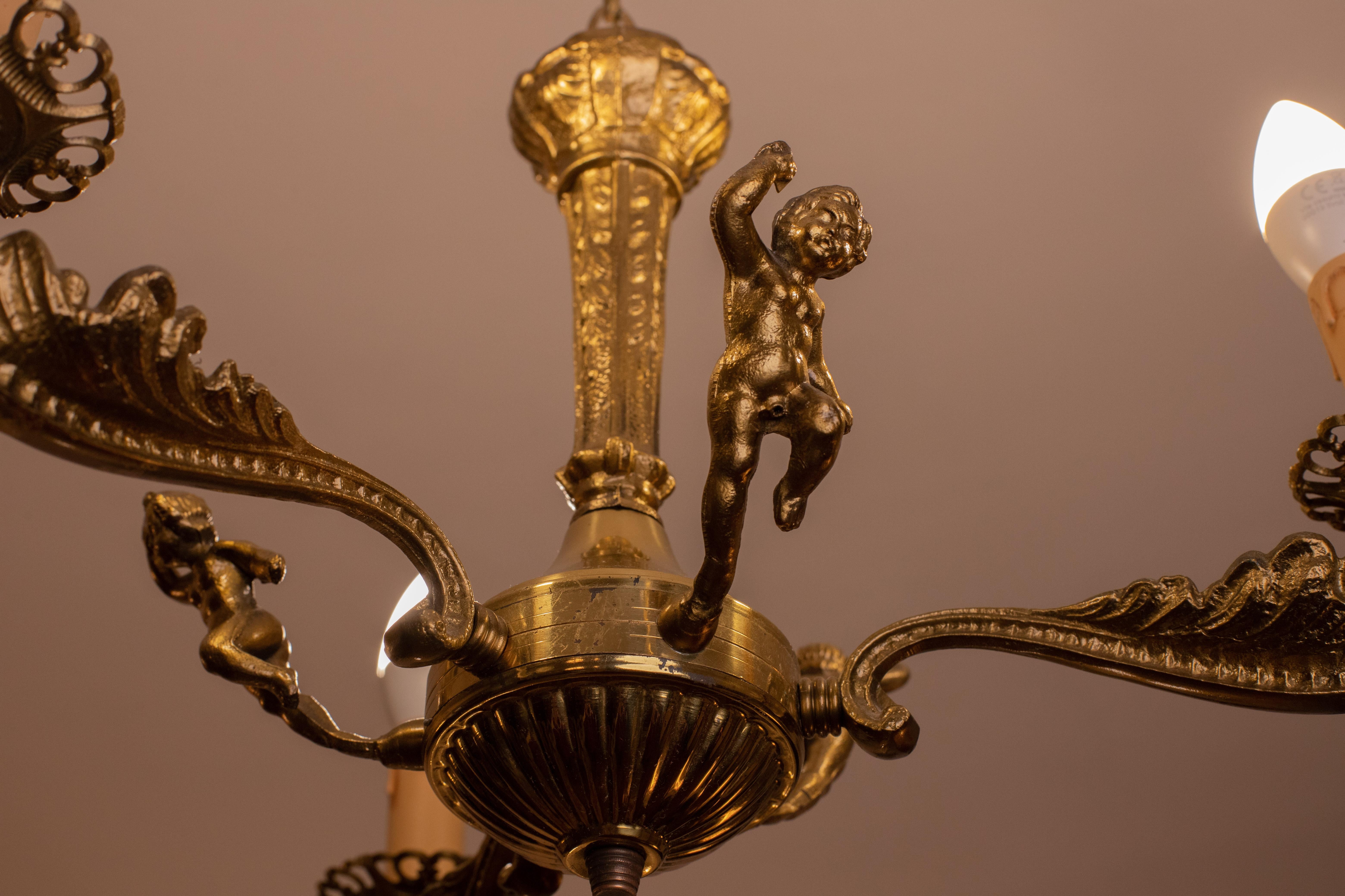 Pretty three-light brass chandelier in Baroque style with three elements depicting a child.
One of the three children (visible in photo) has missing pubis, not visible at all.
The chandelier has 3 arms that mount 3 e14 bulbs, European