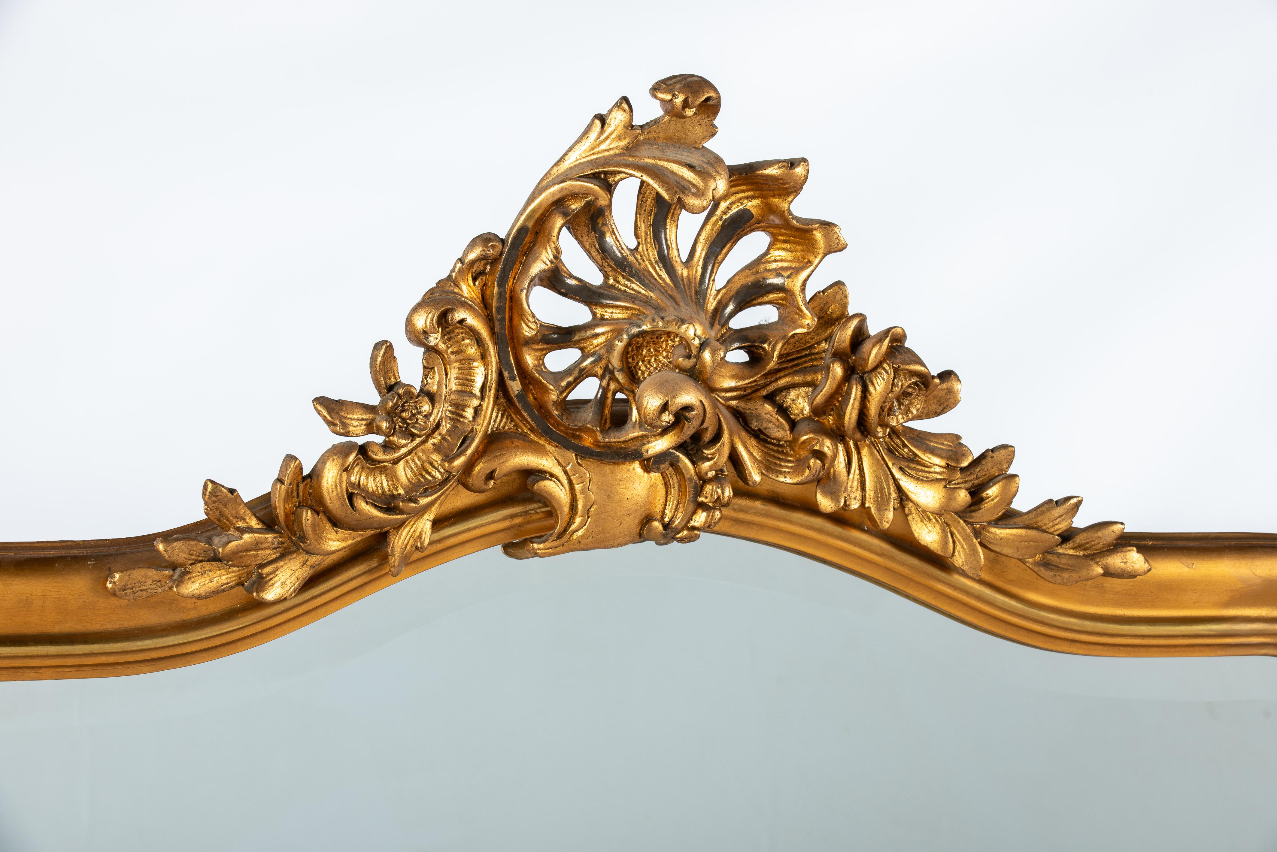 On offer here is a large antique French gold gilded mirror in Louis Quinze or Rococo style. The mirror was made in Northern France in the early 20th century, circa 1900.  It has the asymmetrical ornamentation typical for Louis Quinze and Rococo