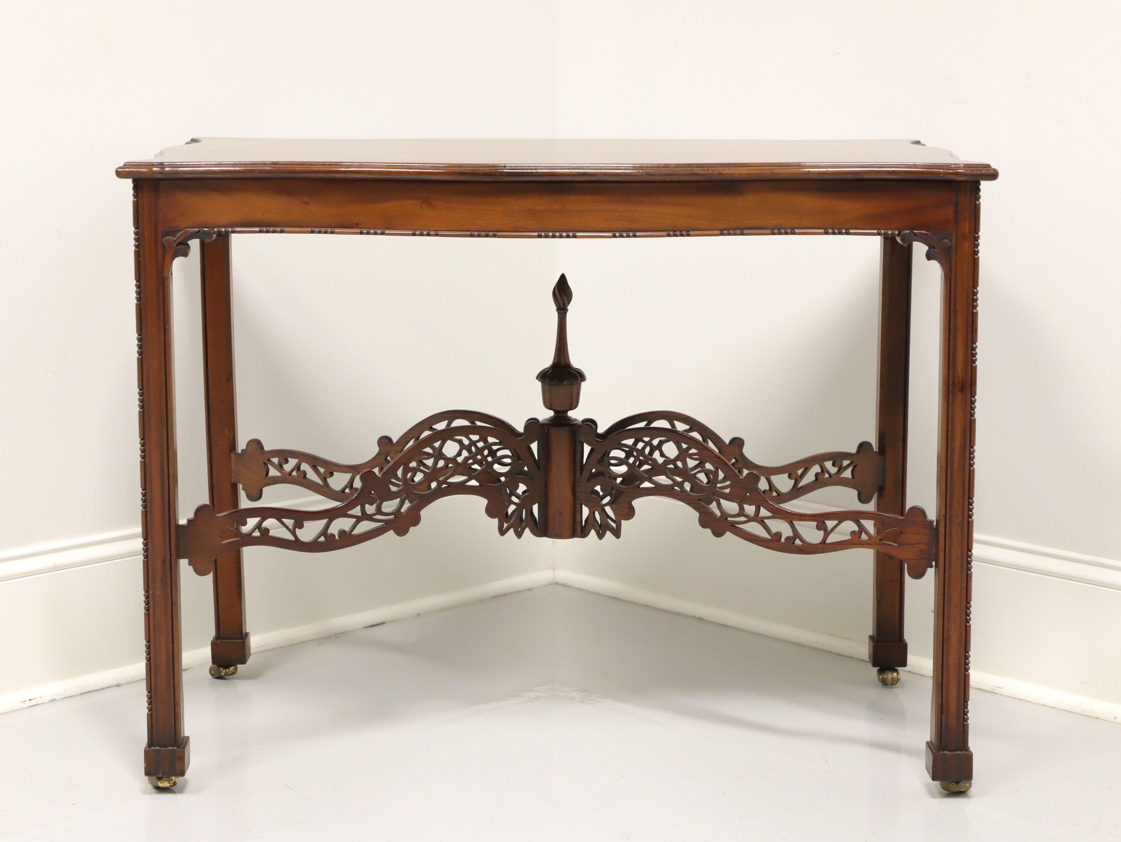 An antique Chippendale style accent table, unbranded, similar quality to Baker. Solid mahogany with brass casters. Features an inlay to top, carved apron, decorative fretwork stretcher base with center finial and carved straight legs. Made in the