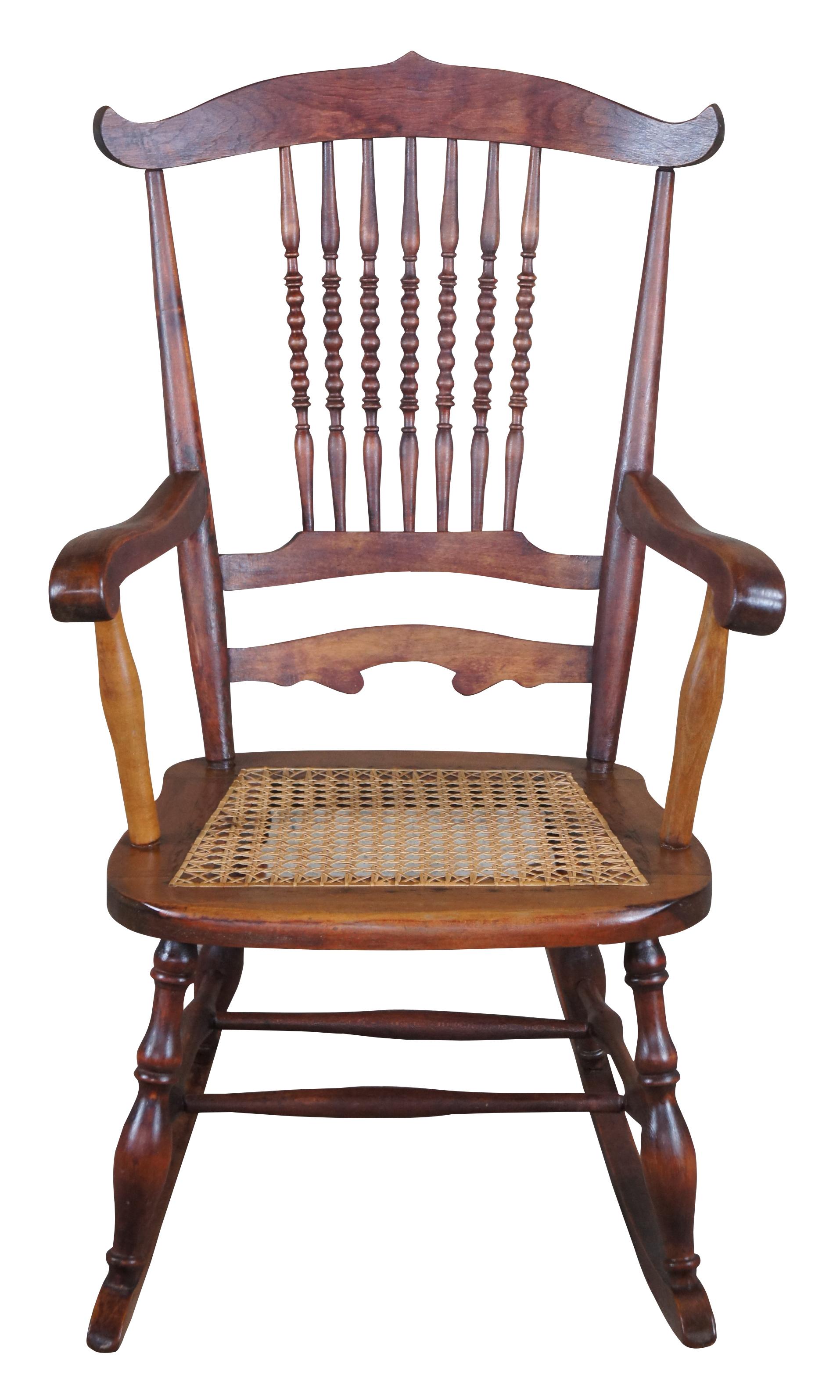 Early 20th century spindle back rocking chair. Made from maple with a shaped crest rail, sausage turned spindles and caned seat. Lower legs are turned and connected by an H stretcher