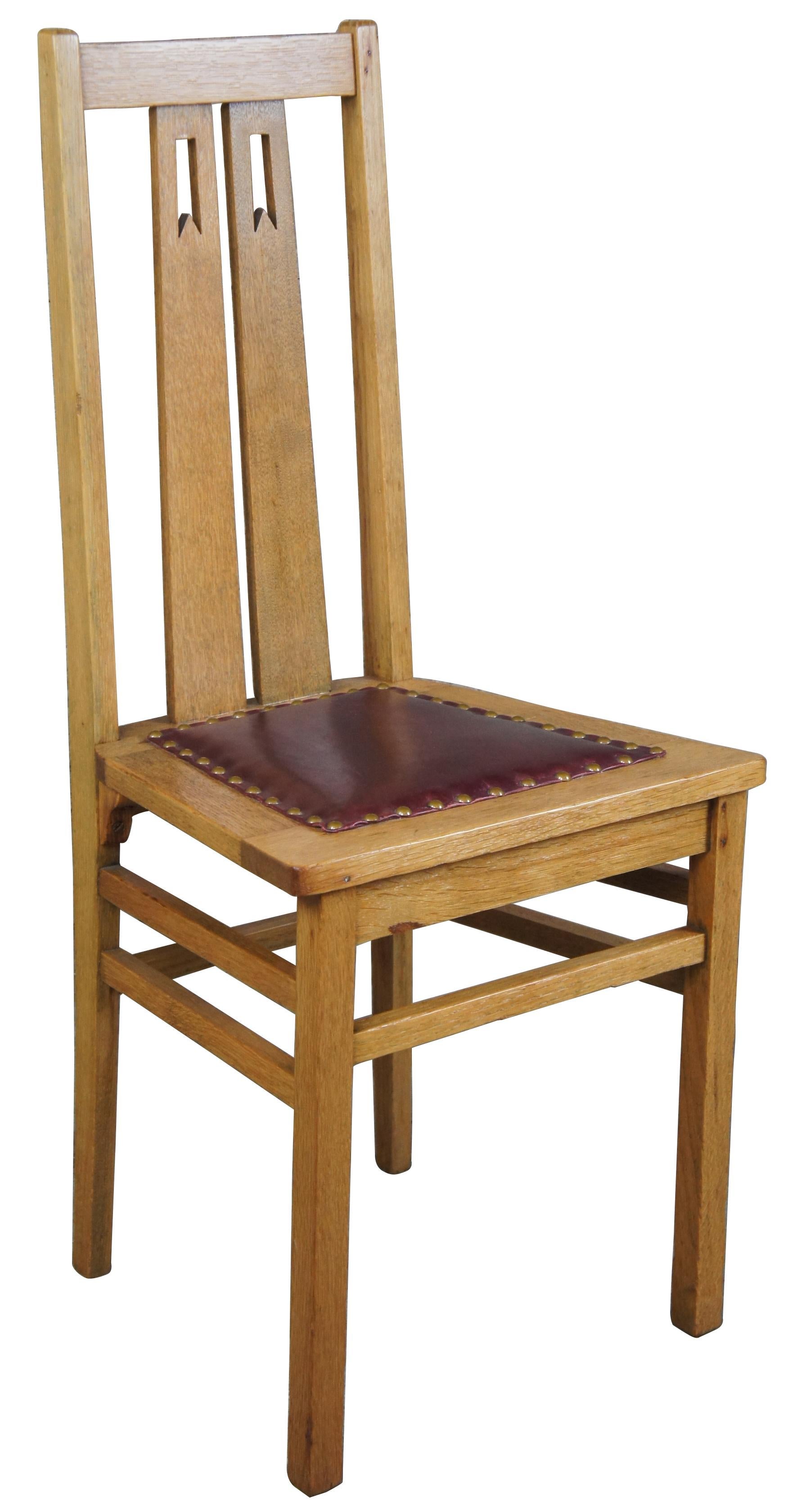 Arts & Crafts oak dining or side chair, circa 1920s. Features a burgundy leather seat with nailhead trim and a pierced rear splats with ribbon design.
  
