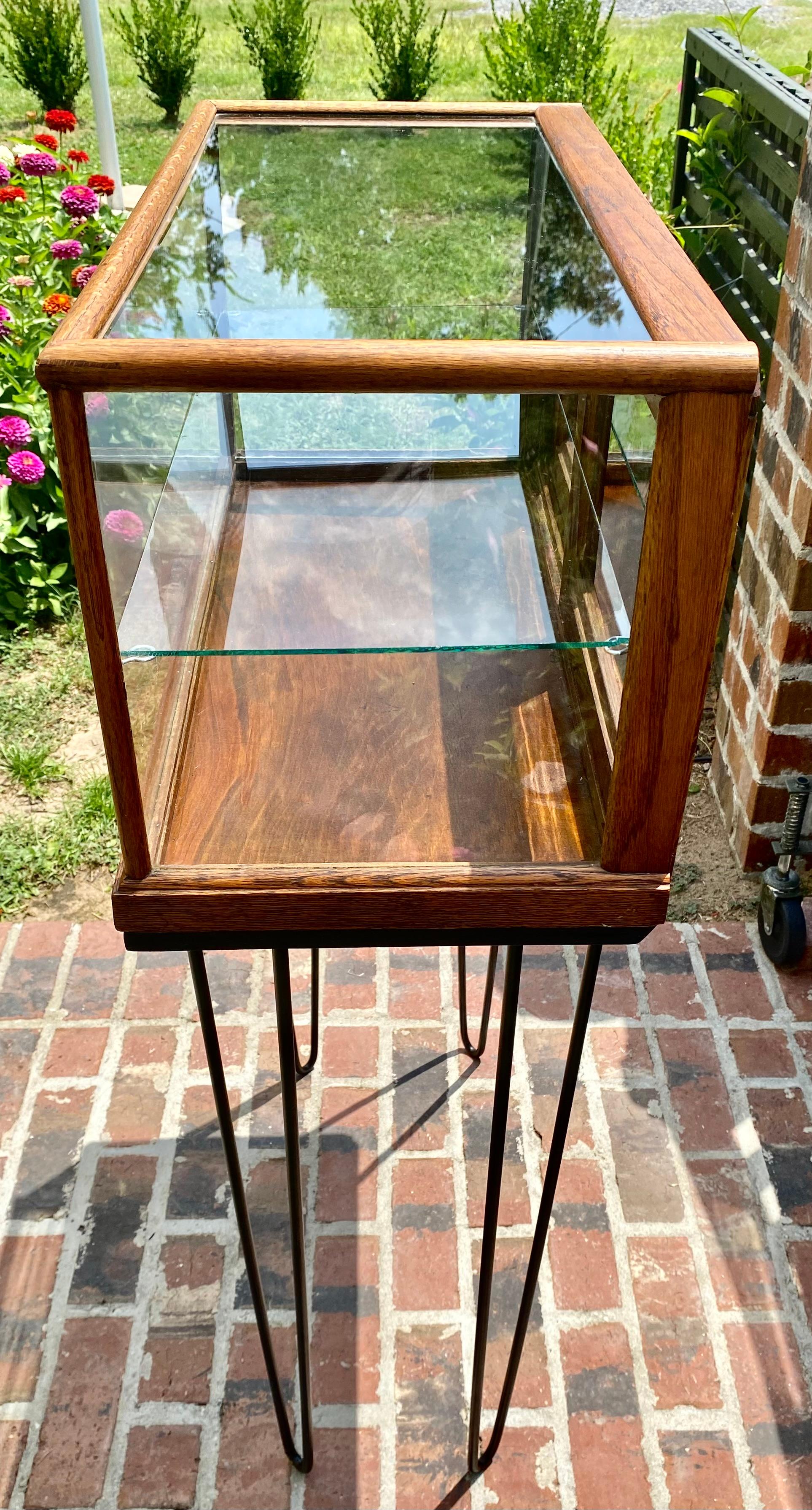 An early 20th century Oak and Glass General store display cabinet having two sliding doors and a glass shelf, now mounted with Iron legs. 

Would make a great dry bar in a small space, home office or study.