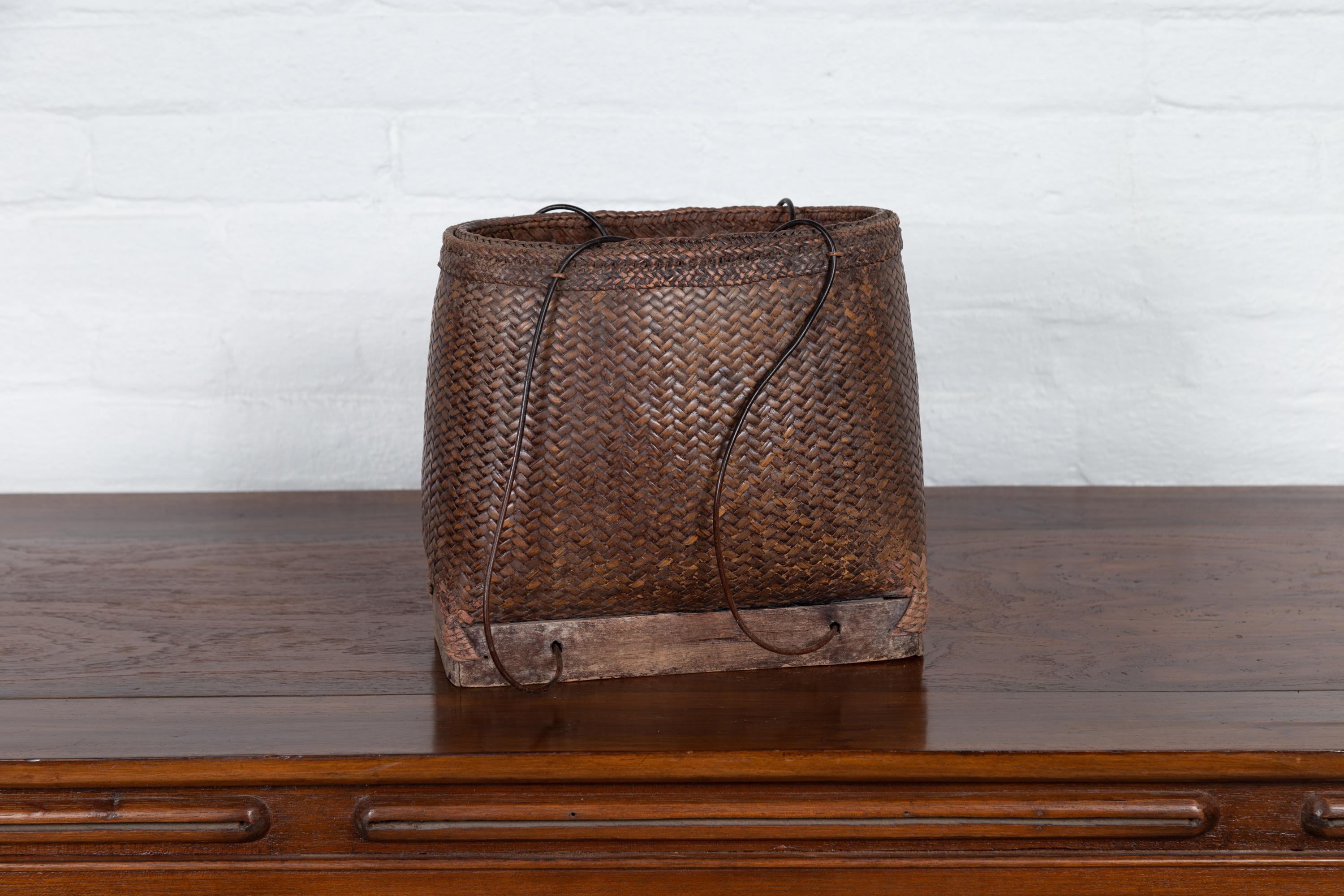 An antique early 20th century small woven carrying grain basket from the Philippines with wooden base. Charming our eyes with its nicely rustic appearance, this woven basket reminds us of the history and use that gives it its charming character.