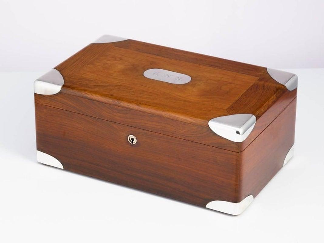 Ein Zigarrenhumidor aus Nussbaumholz aus dem frühen 20. Jahrhundert, CIRCA 1900, mit Sterlingsilberecken und Namensschild.
Dieses Stück hat das Gefühl einer Kampagne, die Ecken sind perfekt geformt.
Die Wände der Box sind mit einem Isolierfilz
