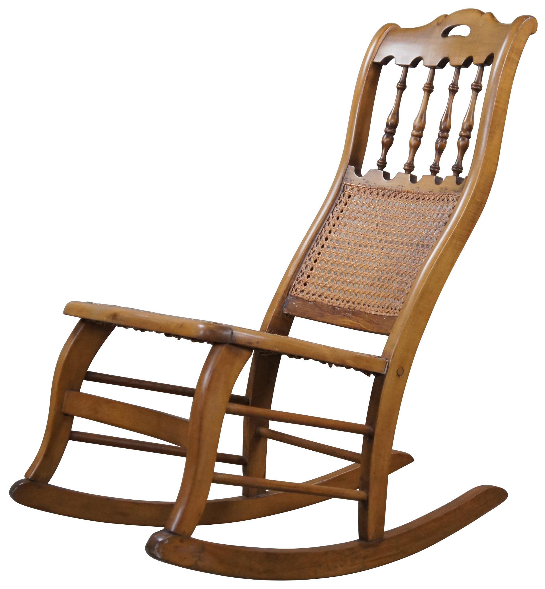 A quaint early American rocking chair, circa 1900s. Made from maple with a spindle back centered between arcade like trim. The chair features a cane seat and back.