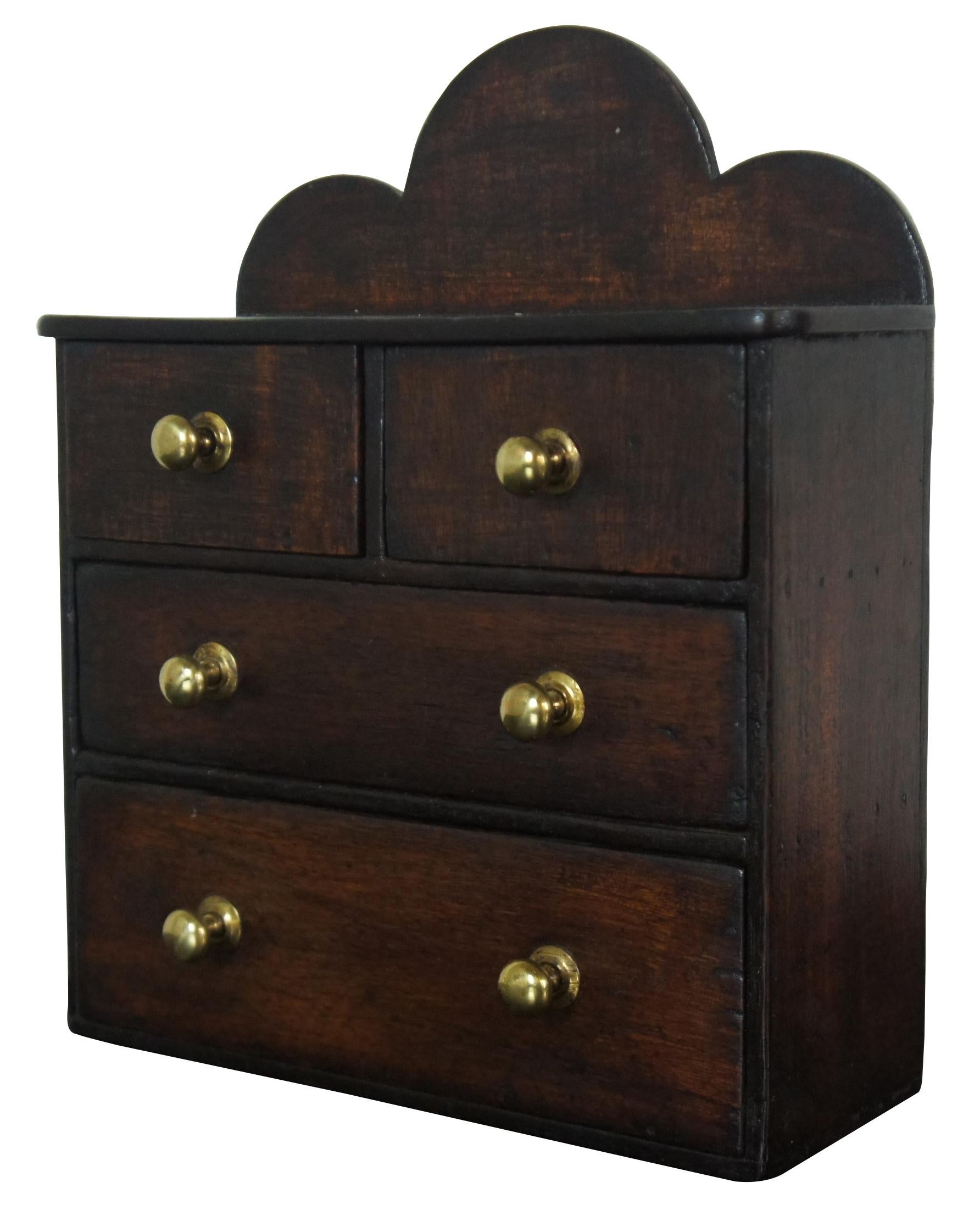 Antique miniature doll sized / salesman sample chest of drawers with brass knobs and a scalloped backsplash.
