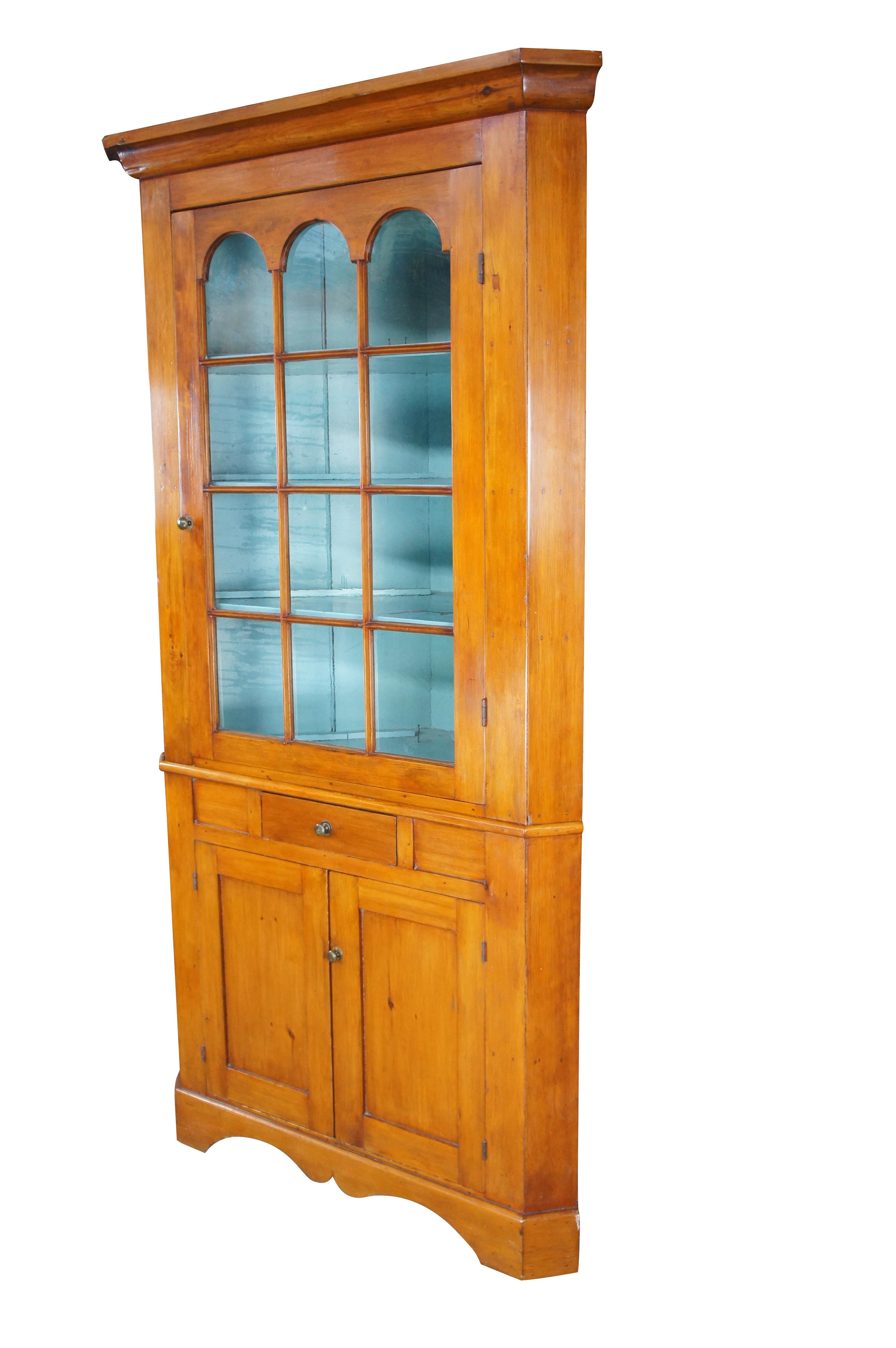 Un antico mobile ad angolo di campagna primitivo americano dell'inizio del XIX secolo.  Realizzata in pino, presenta un'ampia porta ad arco con 12 lastre di vetro laminato che si apre su un interno dipinto di blu con quattro ripiani e scanalature